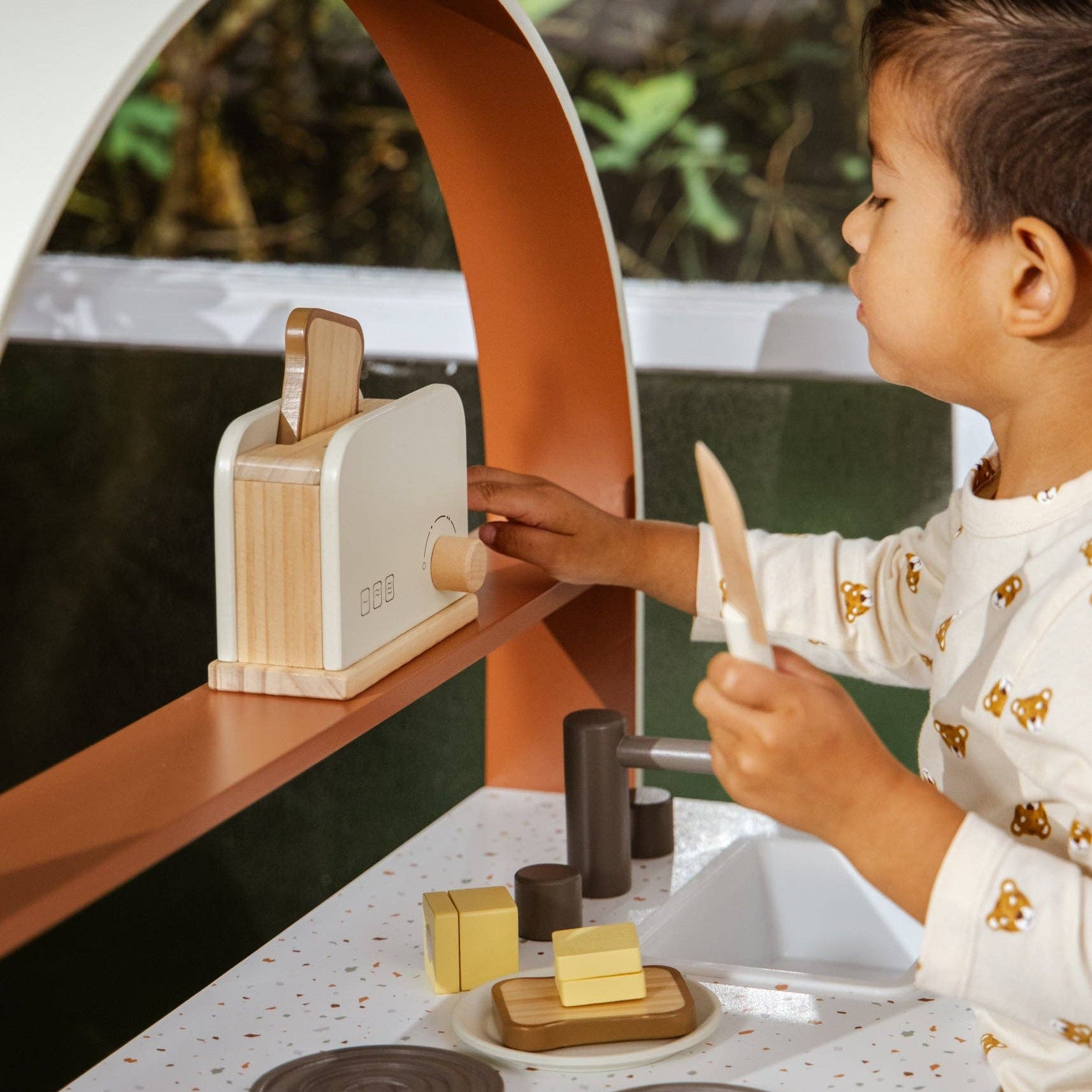 Child playing with a wooden toy kitchen set outdoors