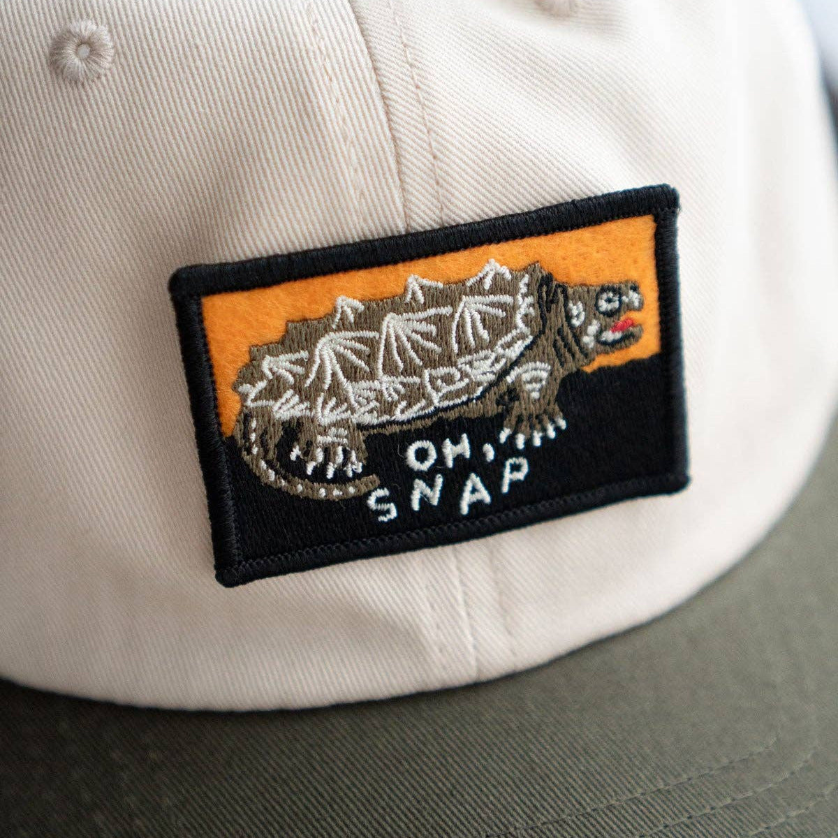 Cap with a patch featuring a snake and 'OH SNAP' text on a beige background