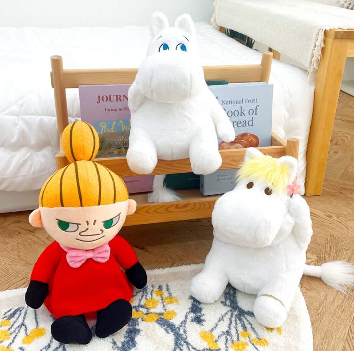 Two plush toys, one resembling a girl with blonde hair and another resembling a white creature, on a wooden floor.