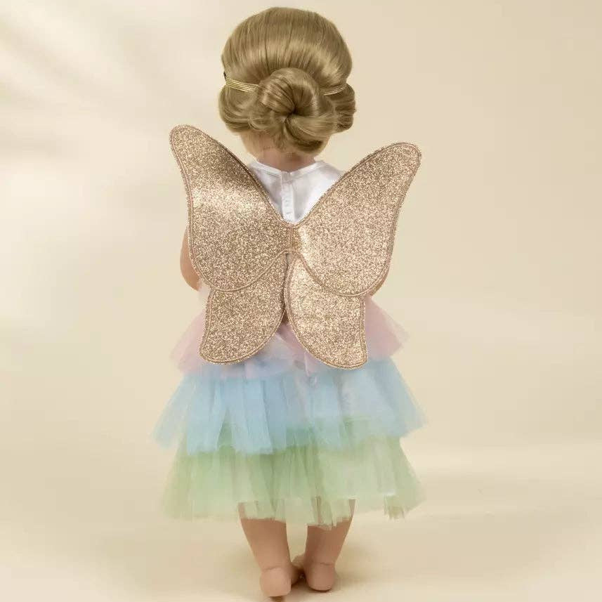 doll wearing a pastel dress with gold butterfly wings on a beige background
