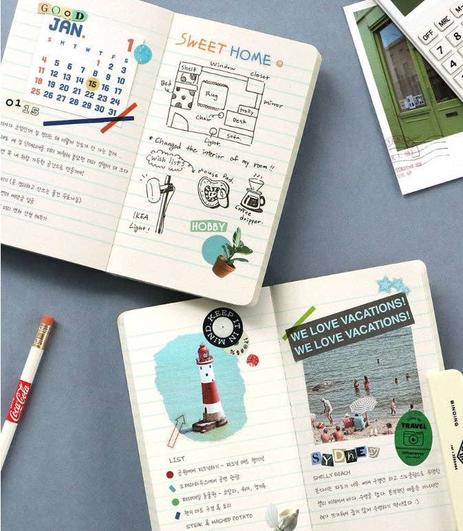 Notebooks with travel-themed pages and a pen on a gray surface