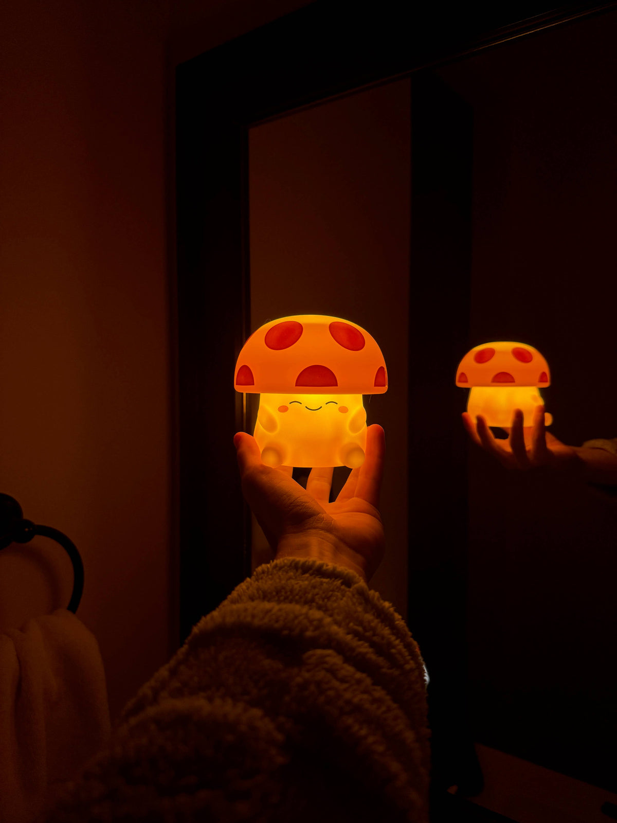 Two glowing mushroom-shaped night lights held in front of a mirror.