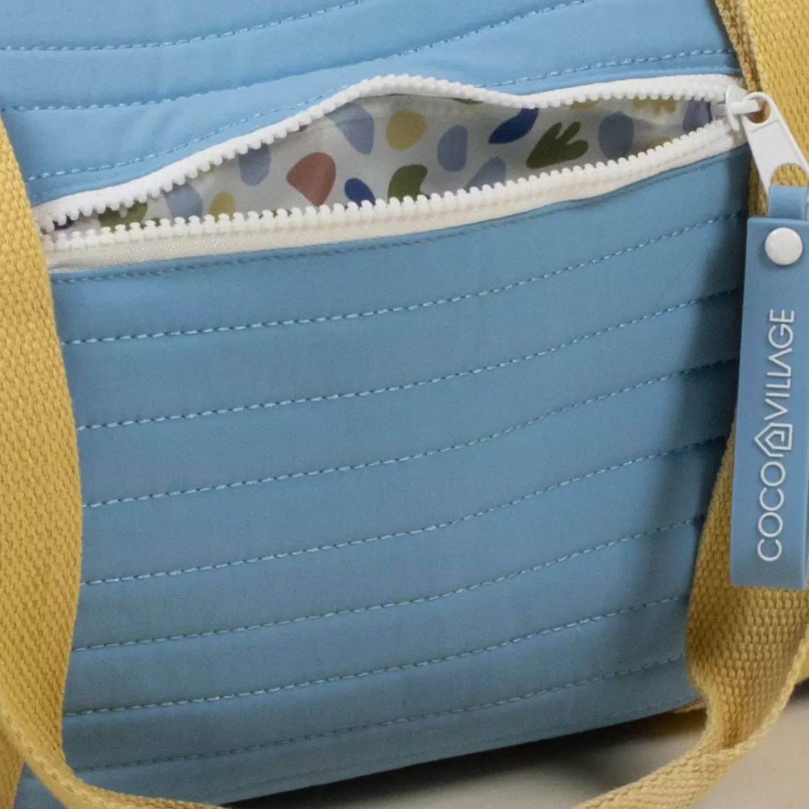 Blue quilted bag with yellow strap and colorful interior lining, featuring a COCO village tag.