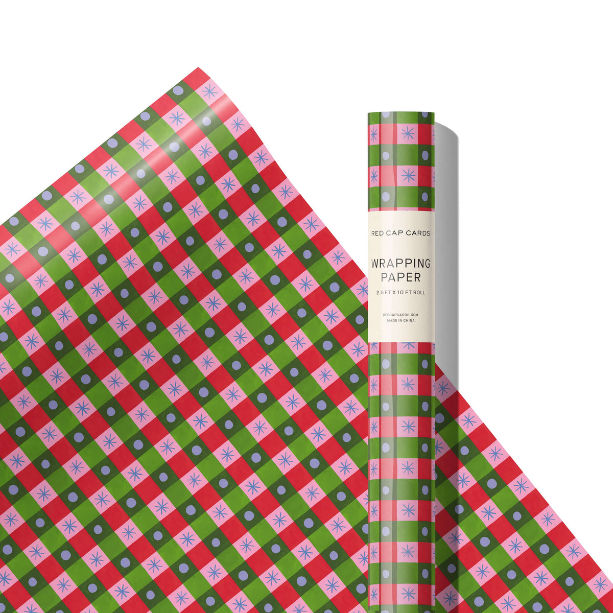 A roll of wrapping paper with a festive red, green, and pink plaid pattern, featuring light blue snowflakes and white polka dots. The paper is partially unrolled to display its pattern, with the roll standing upright next to it on a clean white background.