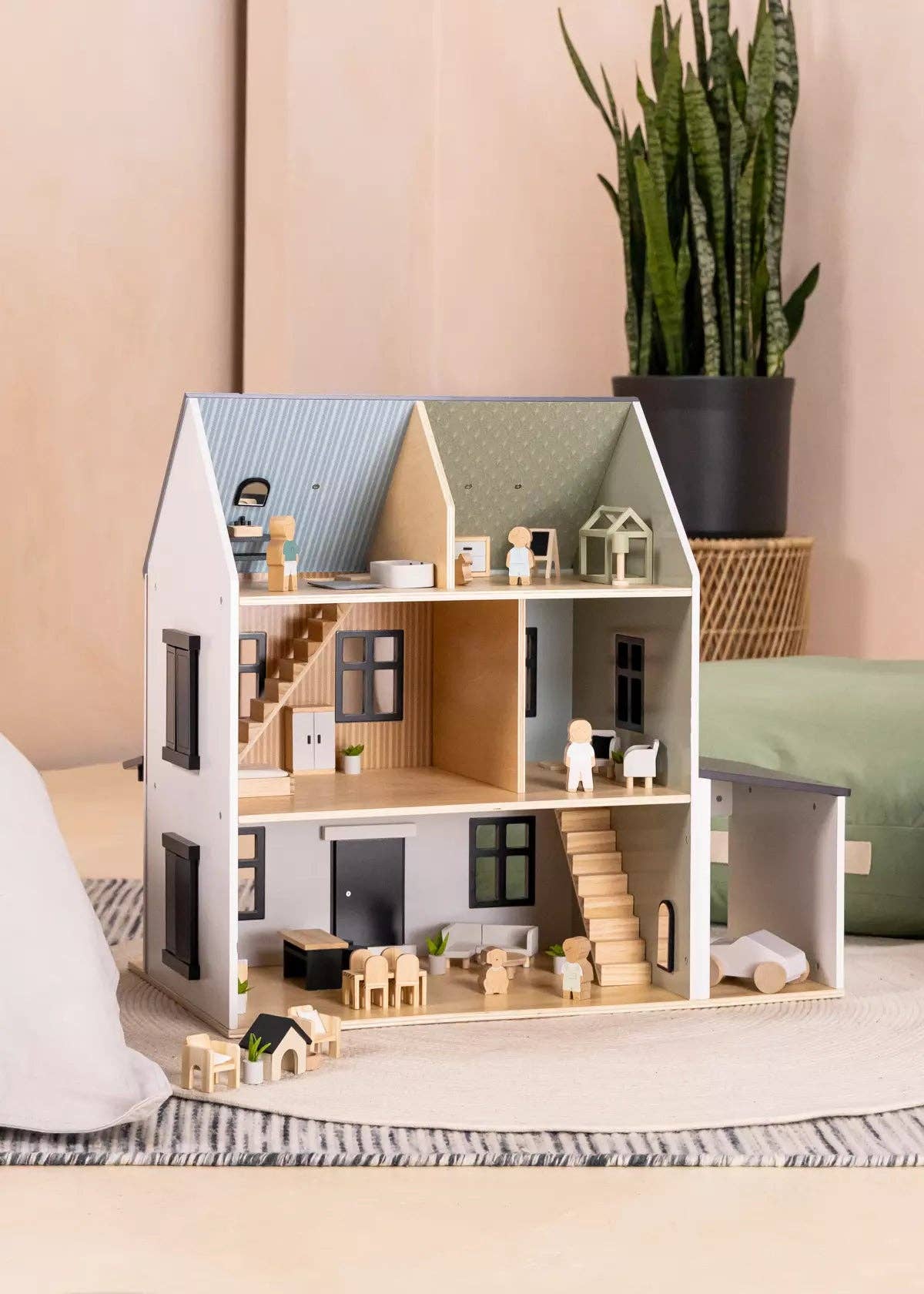 Wooden dollhouse with furniture on a bed against a beige wall with a plant.