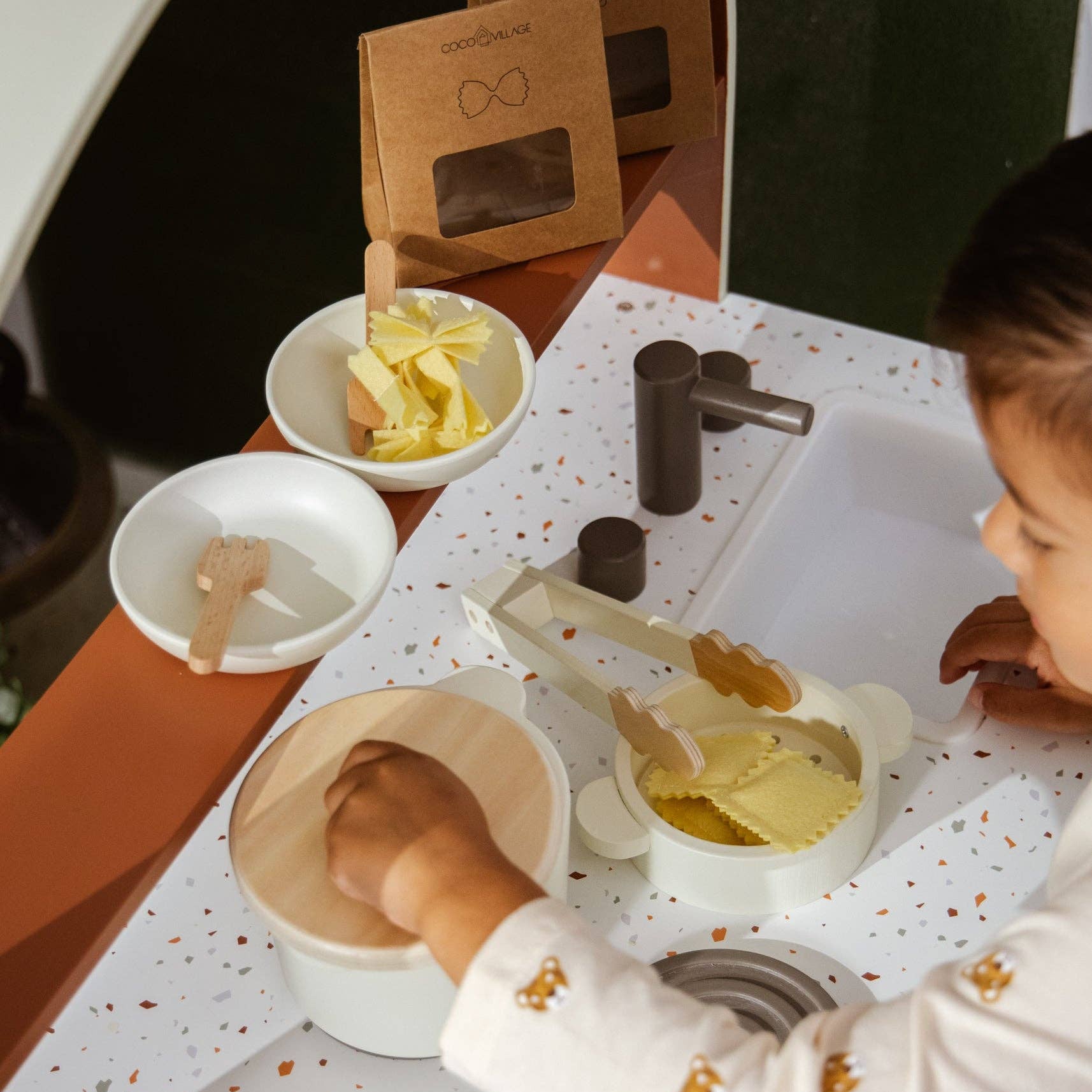 Child playing with play dough at a table with various play items.