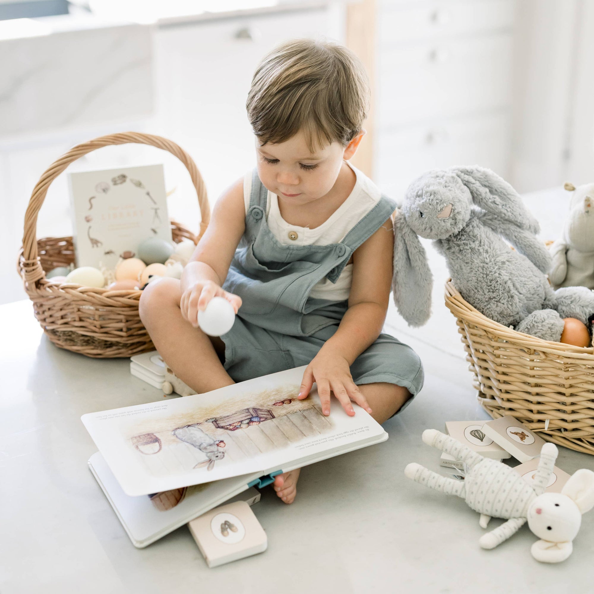 Child reading a book with toys around in a bright room