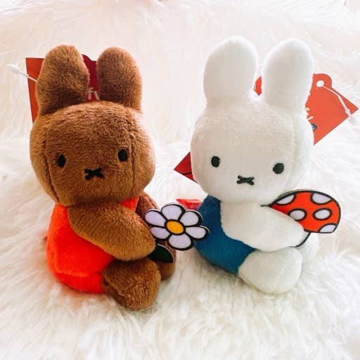 Two plush toys, one brown and one white, sitting on a white surface.