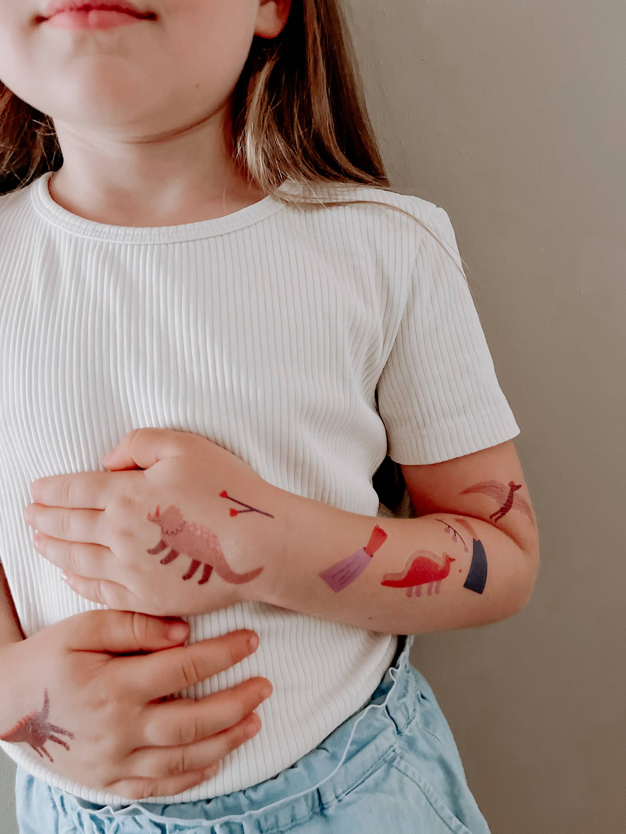 Child with temporary tattoos on arms and hands against a neutral background