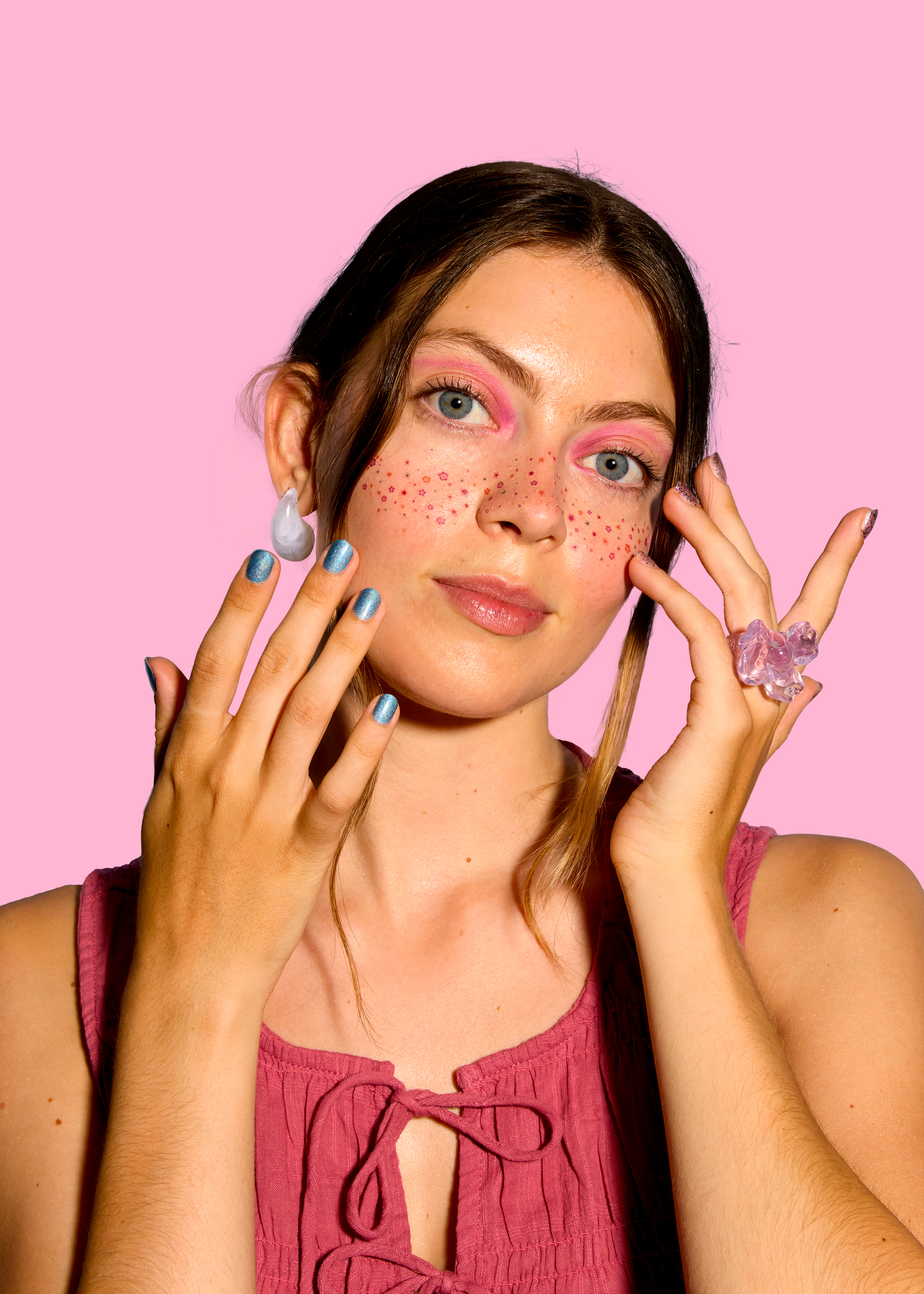 Woman with pink makeup and nail polish against a pink background