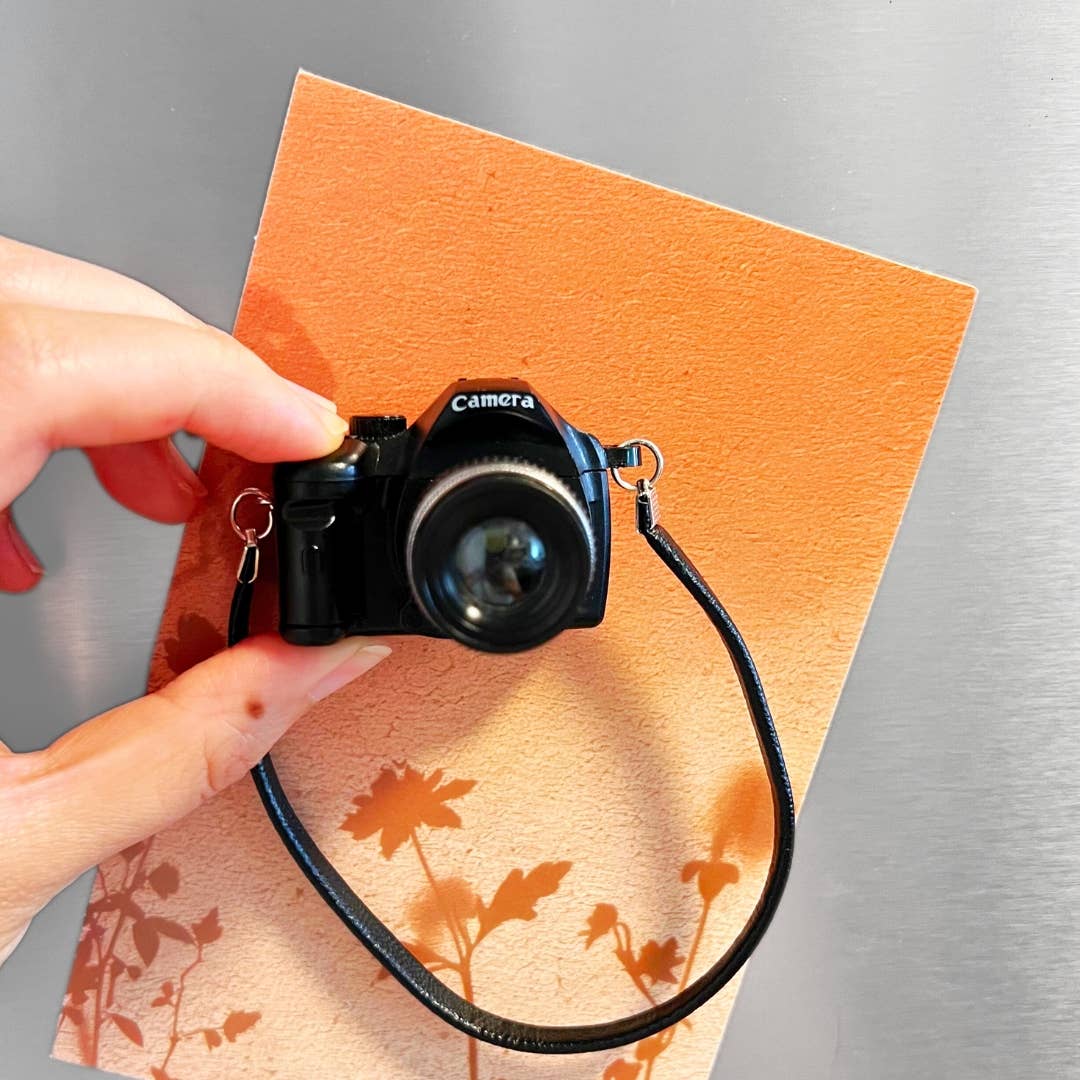 Small camera held by a hand on an orange surface with floral patterns