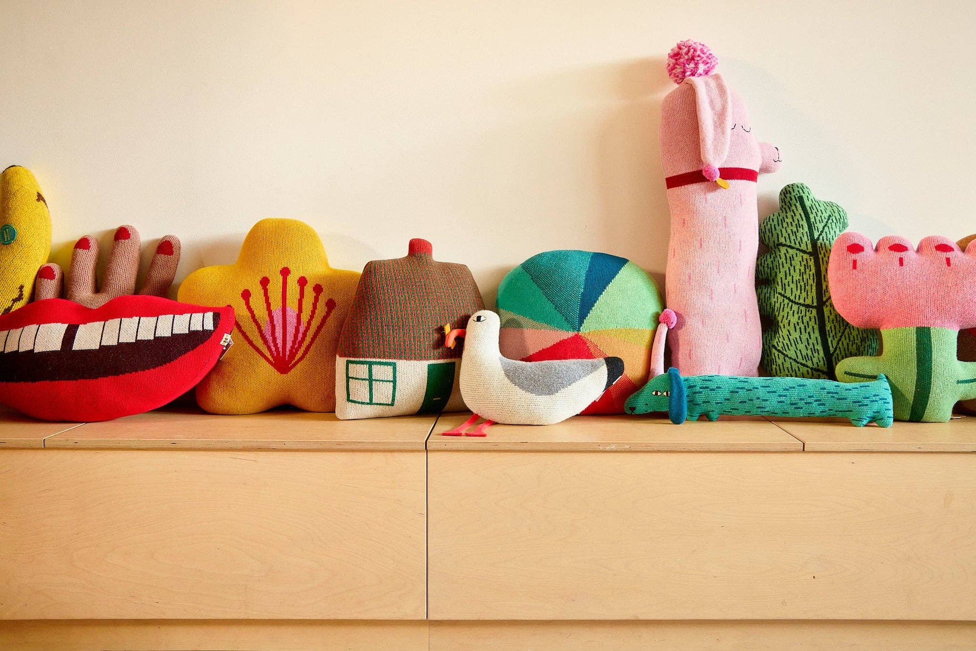 Colorful plush toys arranged on a wooden shelf against a light background