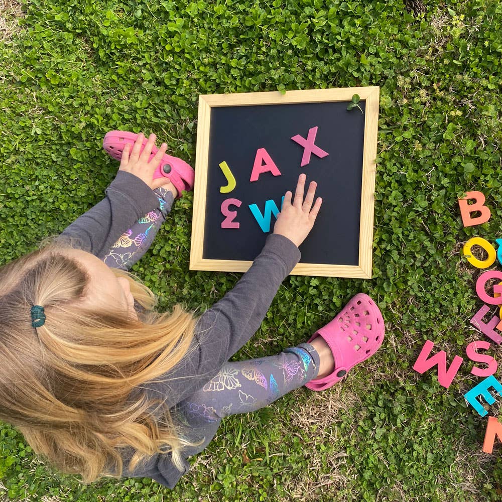 Child playing with colorful letters on a blackboard in the grass