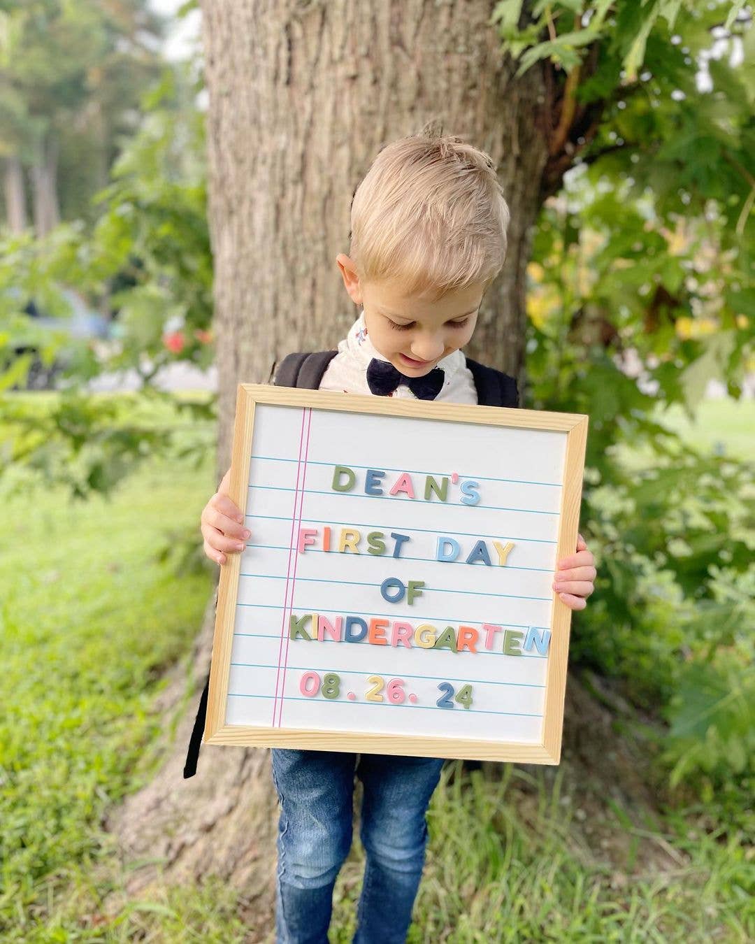 Child holding a sign for their first day of kindergarten outdoors.