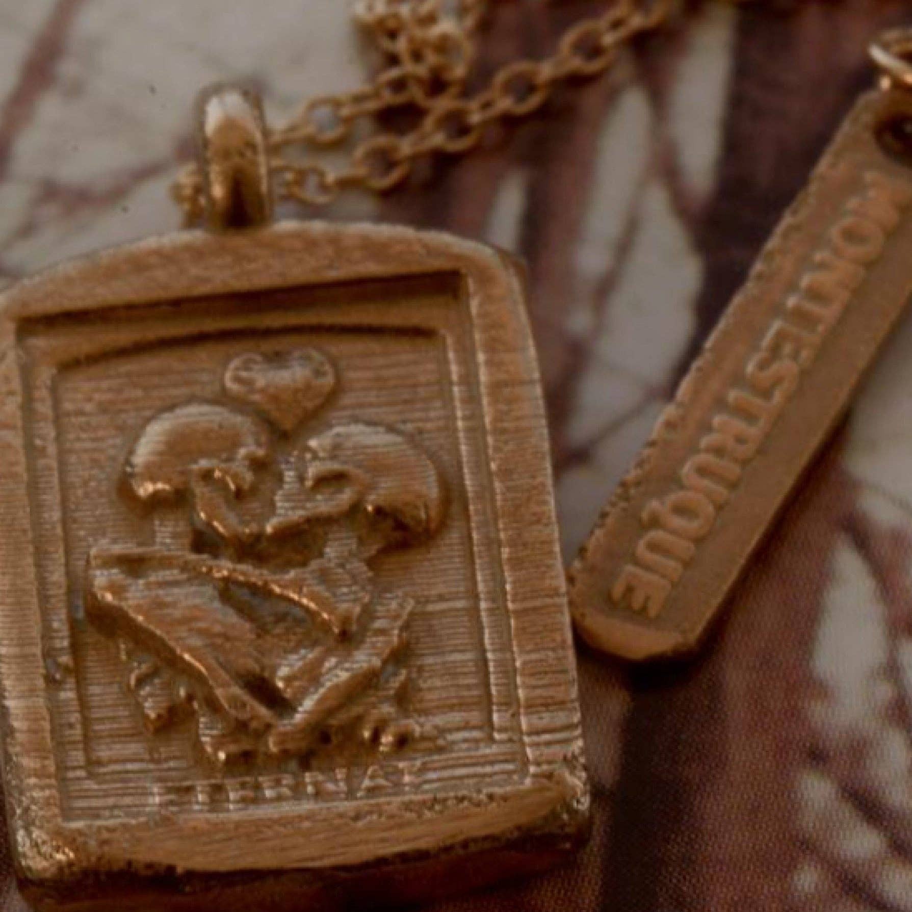 Two gold pendants with engraved designs on a textured surface