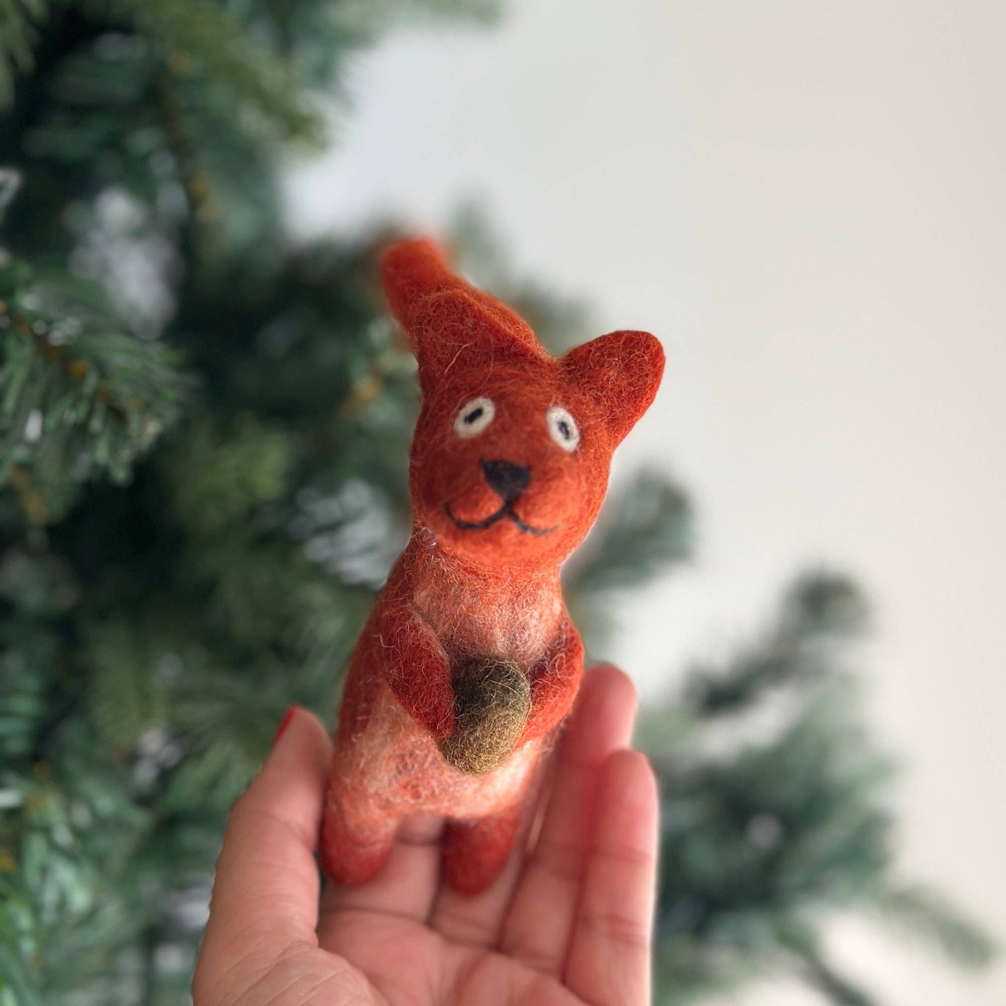 Hand holding a small red fox plush toy with a blurred green tree background