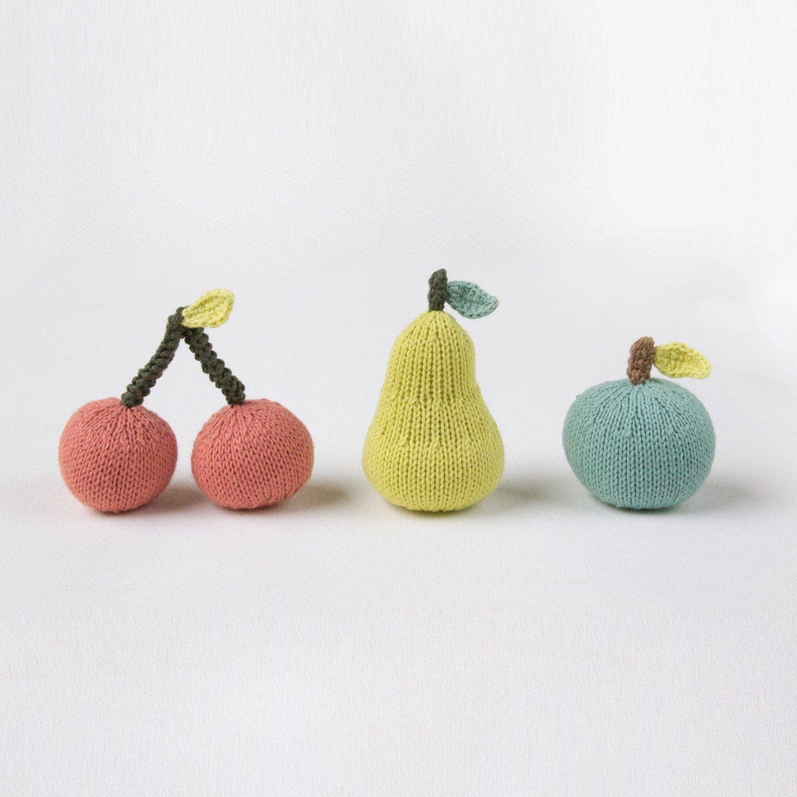 Knitted toys shaped like a cherry, pear, and apple on a white background