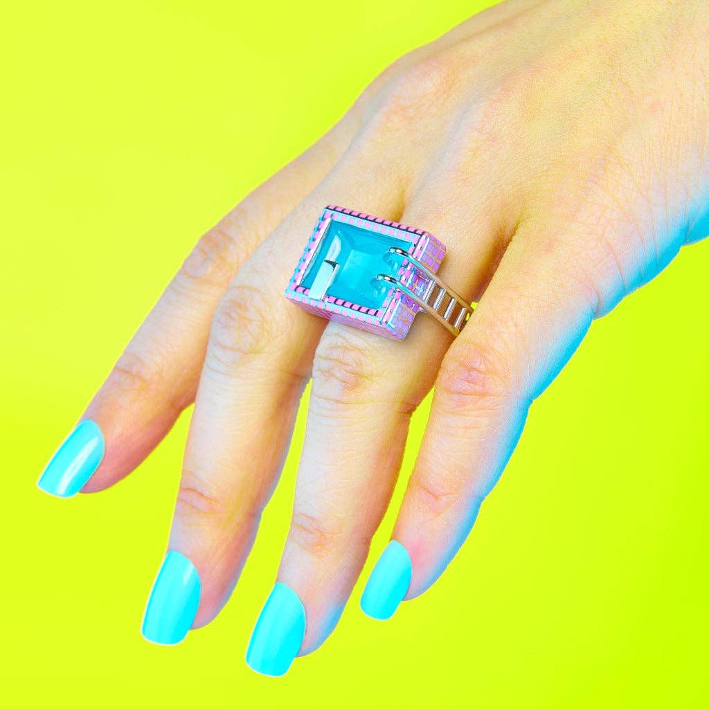 Hand wearing a colorful ring with a blue gemstone against a bright yellow background