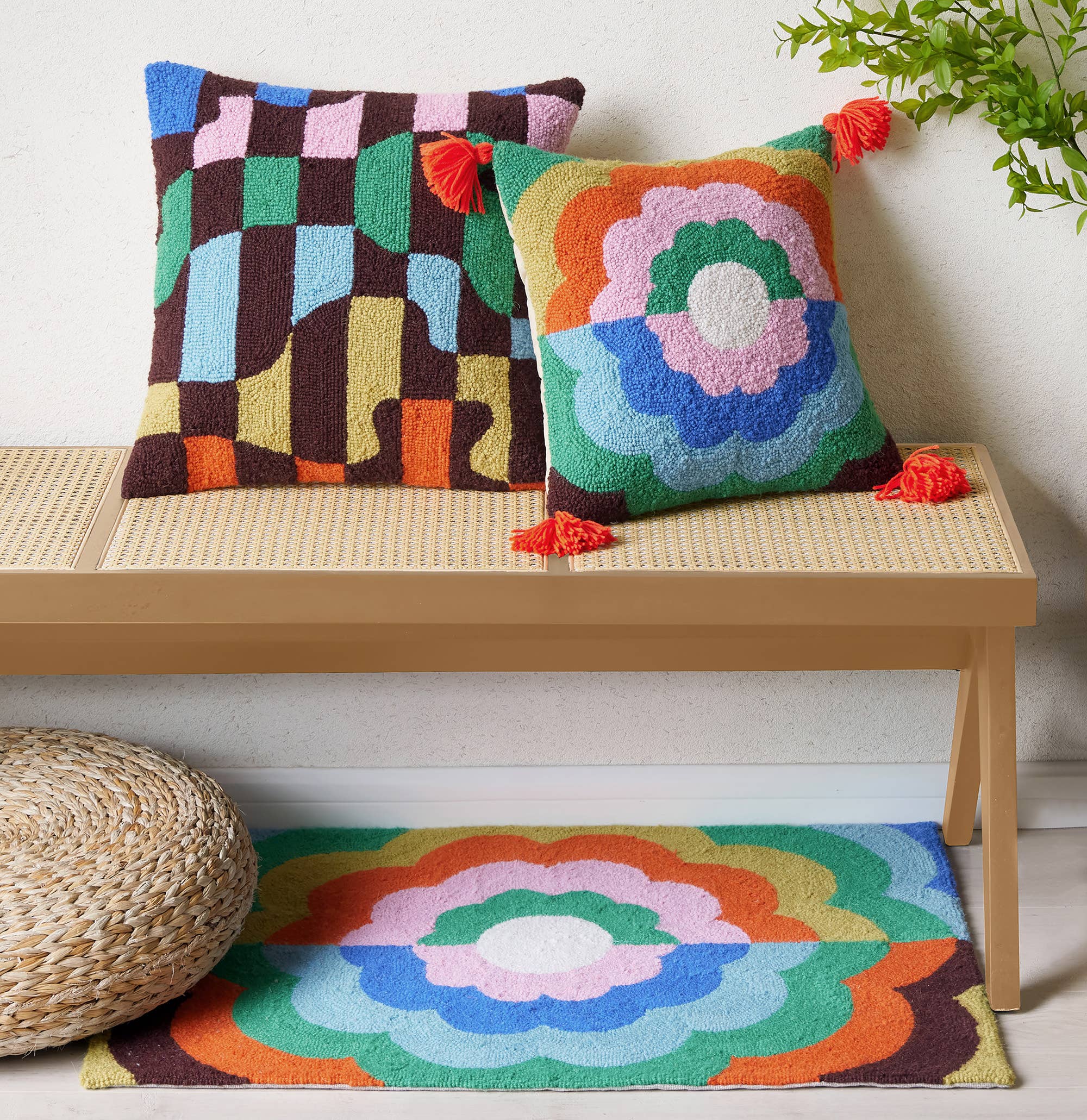 Colorful patterned cushions and rug on a wooden bench with a plant in the background.