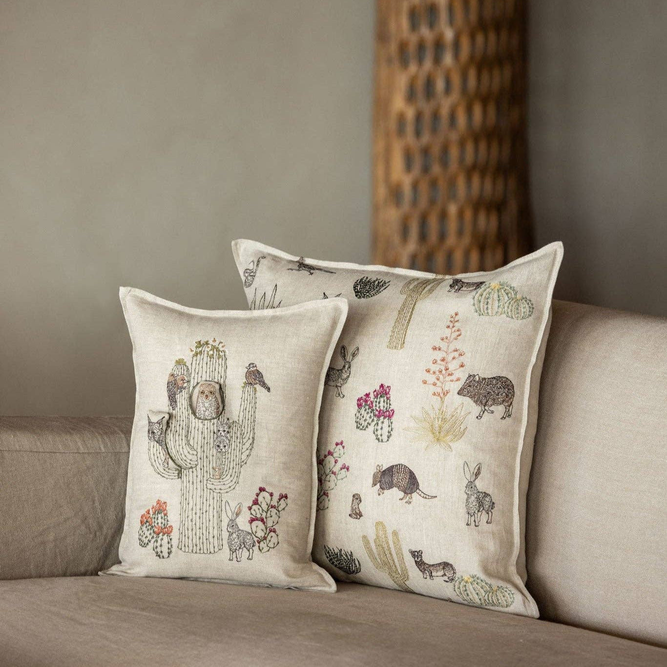 Decorative pillows with cactus and desert animal designs on a beige sofa.