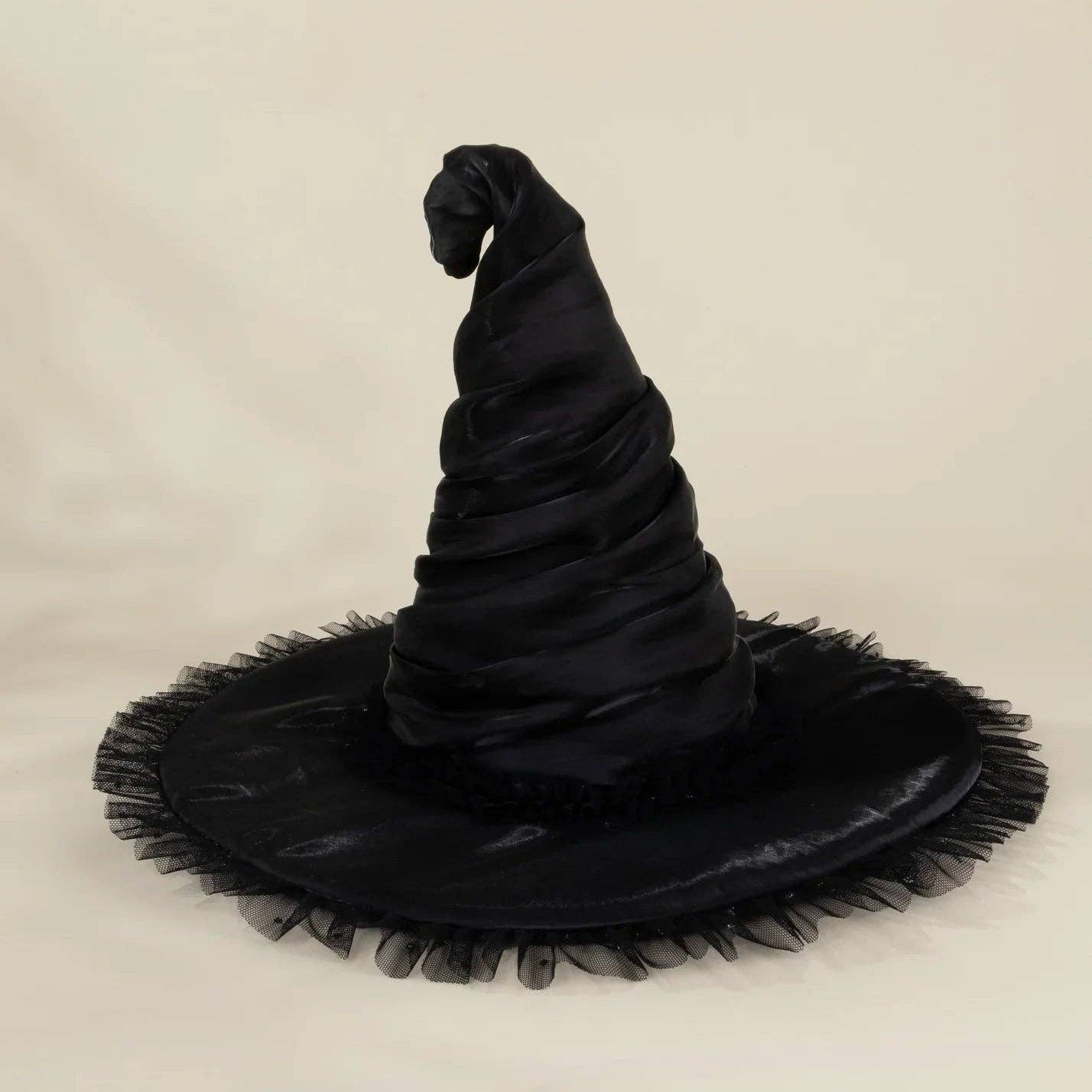 A black witch hat with a wide, frayed brim, photographed against a plain light beige studio background.