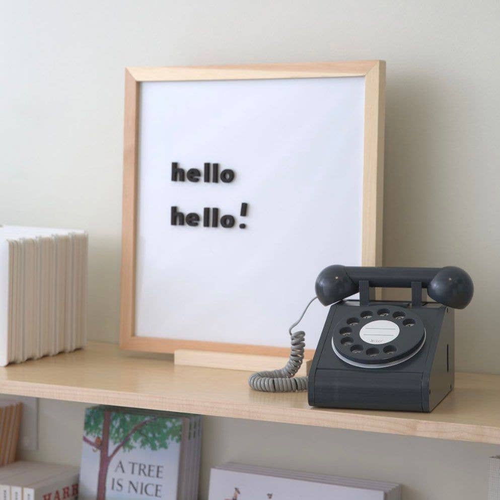 Vintage black rotary phone on a wooden shelf with a framed picture displaying 'hello hello!'.