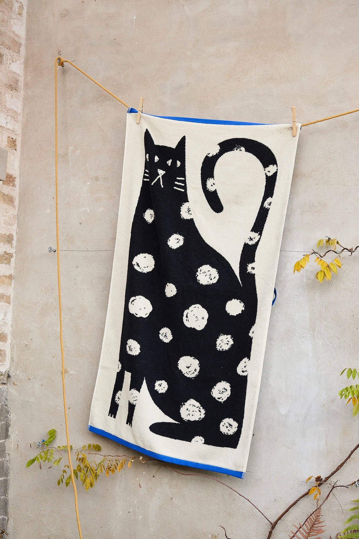 Towel with a black cat design hanging on a line against a concrete wall.