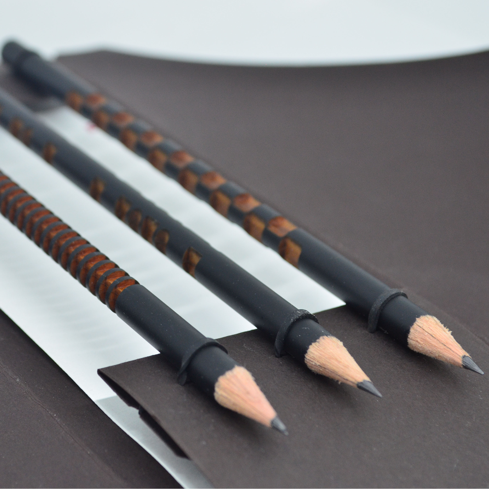Three black makeup pencils with brown accents on a brown surface