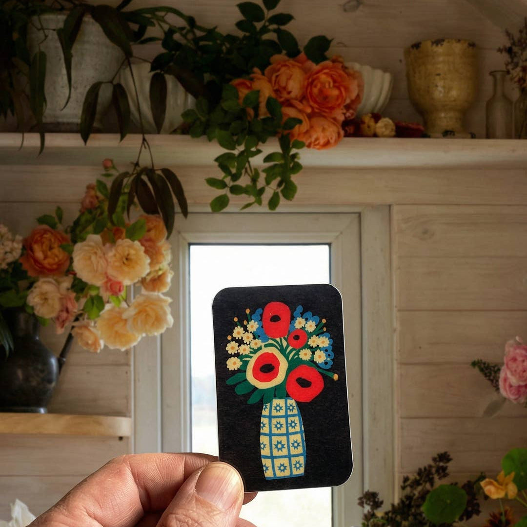Hand holding a small embroidered patch with floral design in a home setting with flowers and decor.
