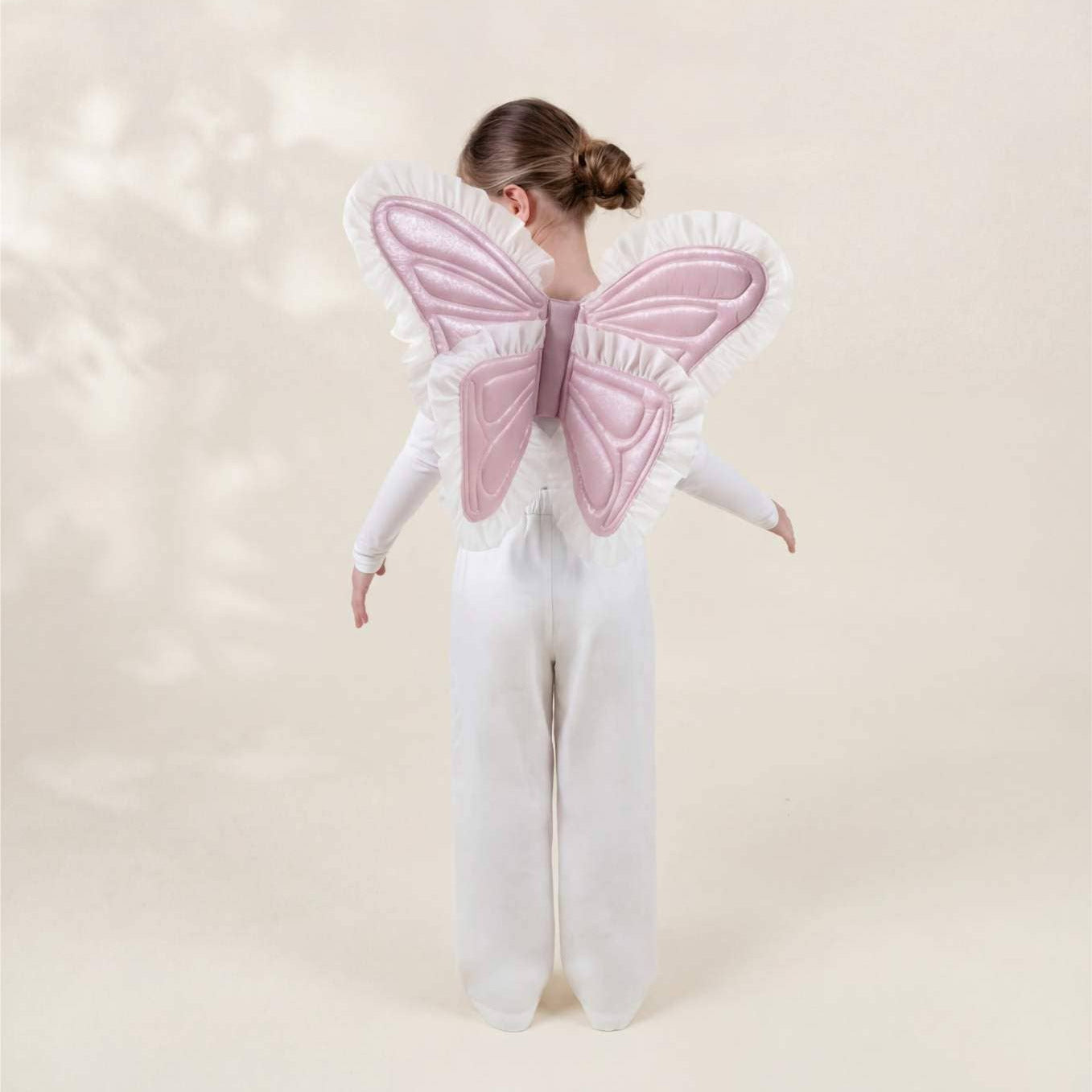 Person wearing a white outfit with pink butterfly wings on a light background
