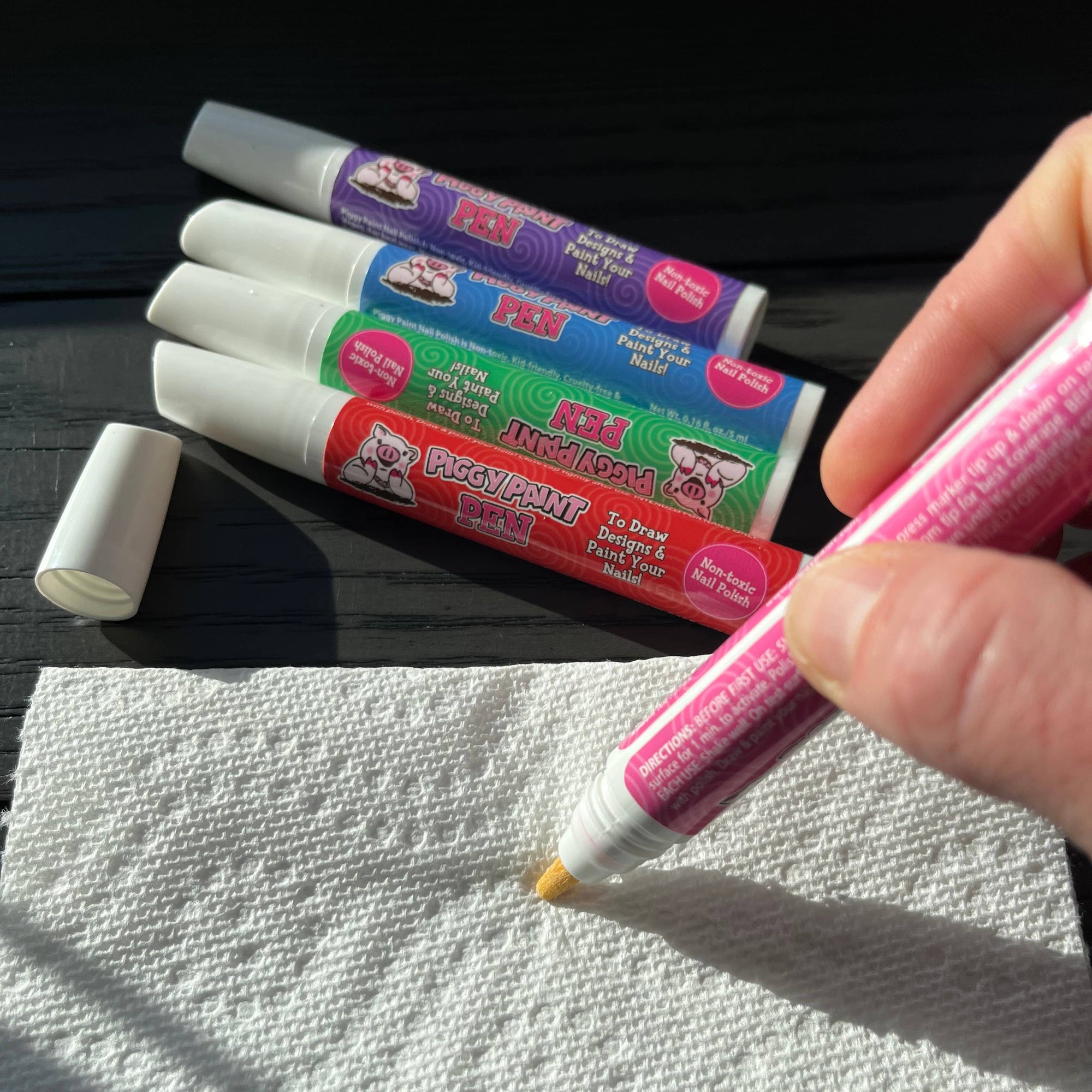 Pink marker being used on a white paper towel with other markers in the background.