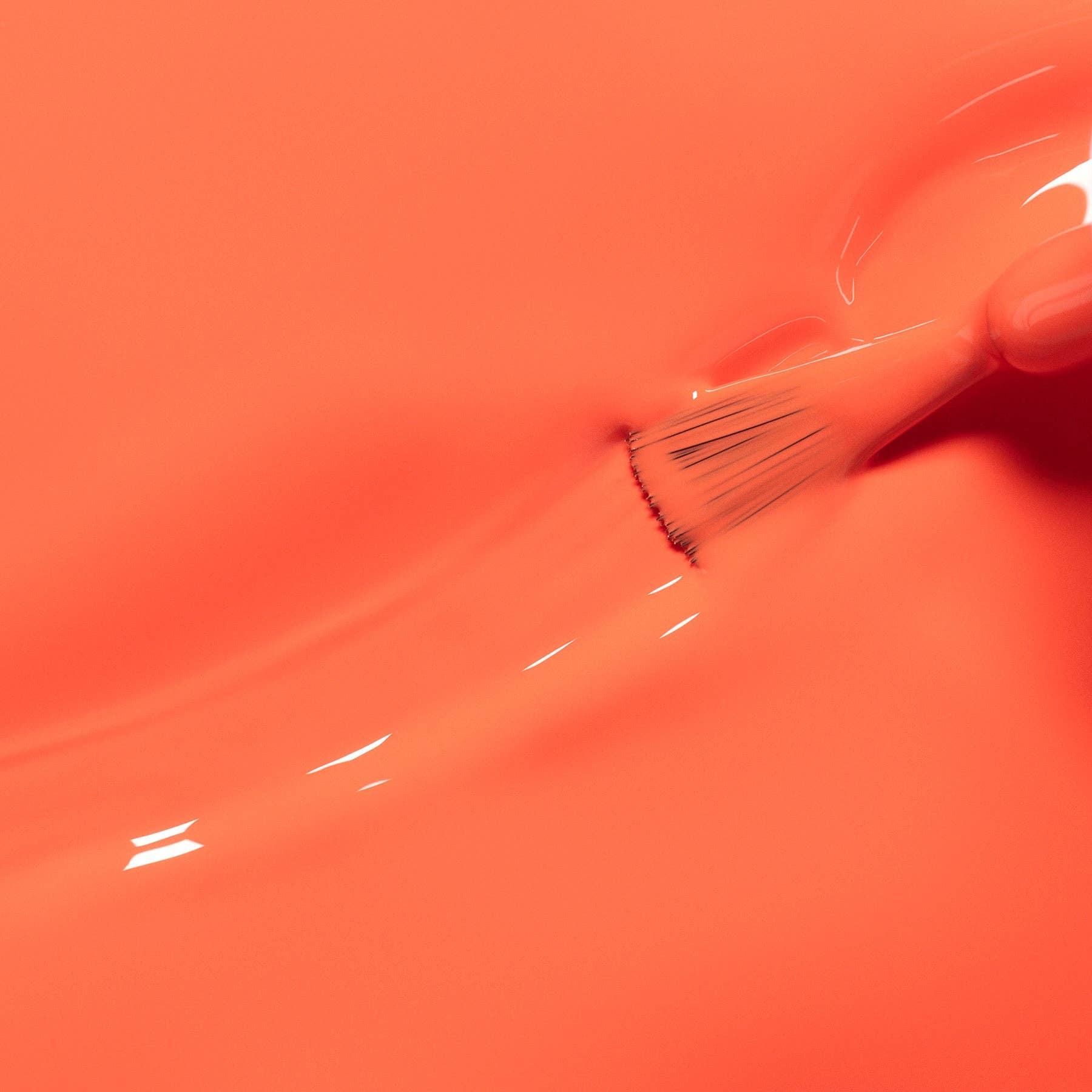 A close-up of glossy coral-orange nail polish with a brush stroke and a small fingernail visible, showing the saturated color finish.