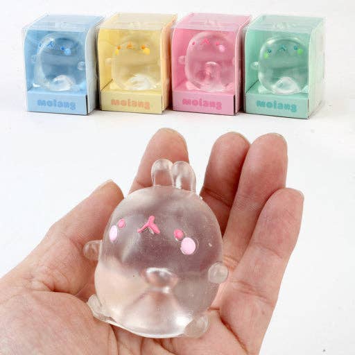 Clear gelatinous toy with pink accents held in a hand, with colorful boxes in the background.