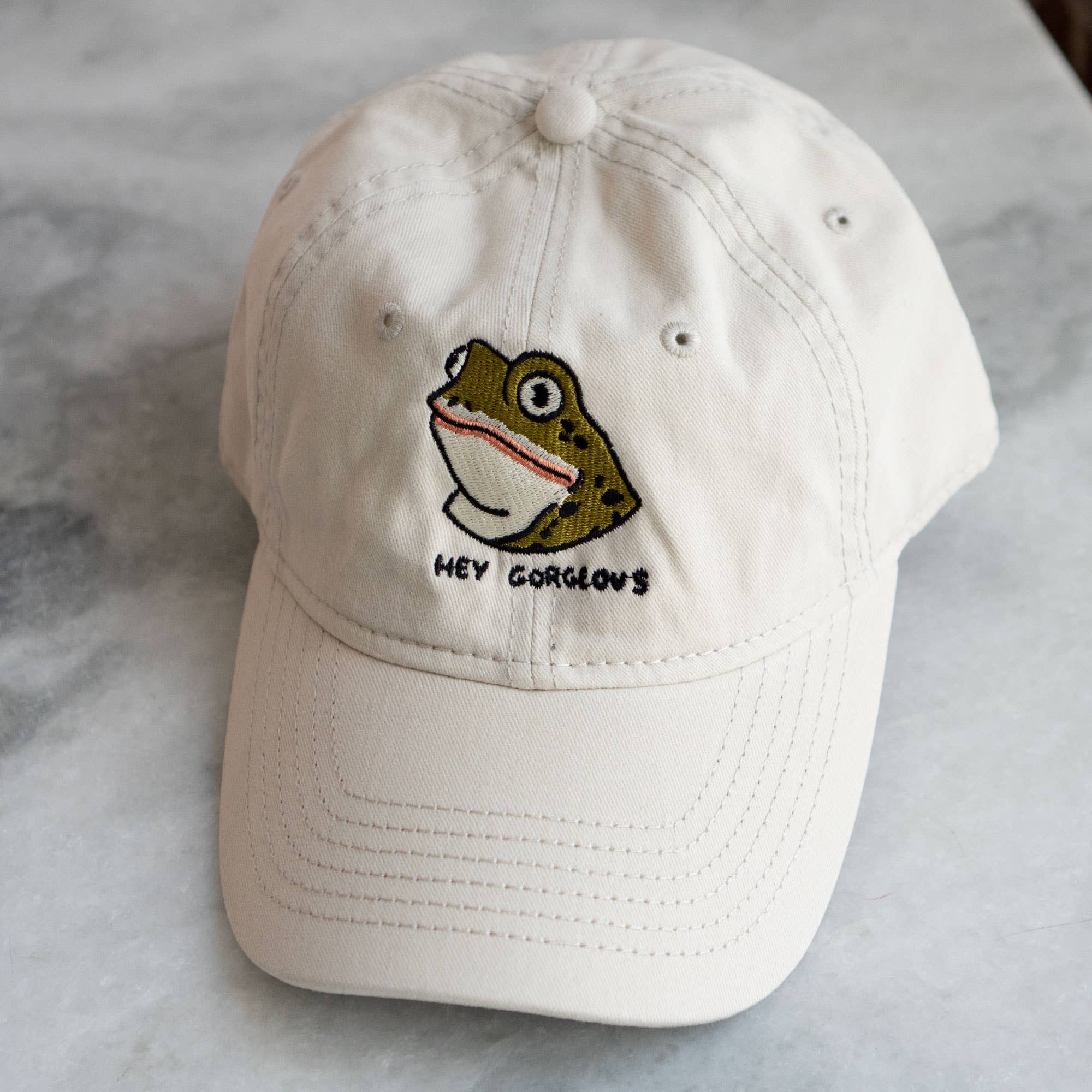 White cap with a frog design and text on a marble surface