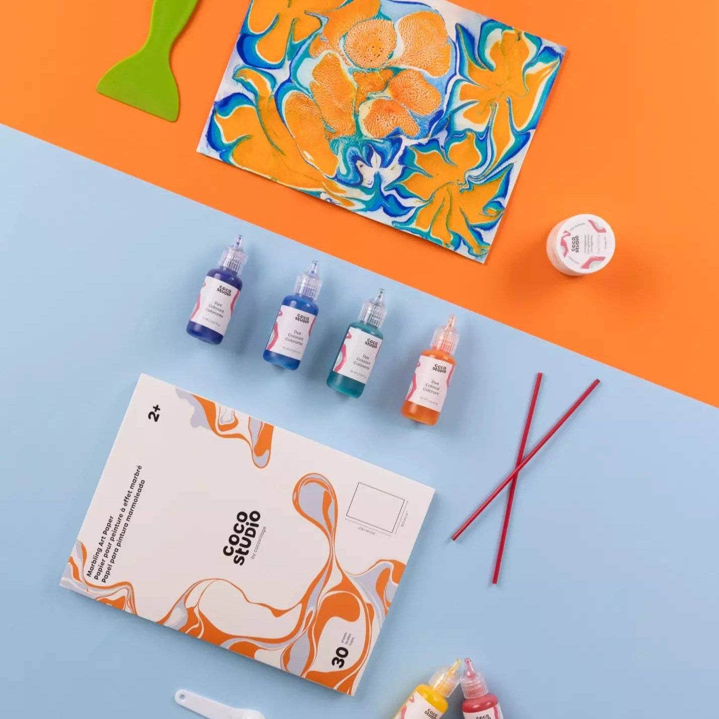 Art supplies including a paint palette, bottles of paint, and a book on an orange and blue background.