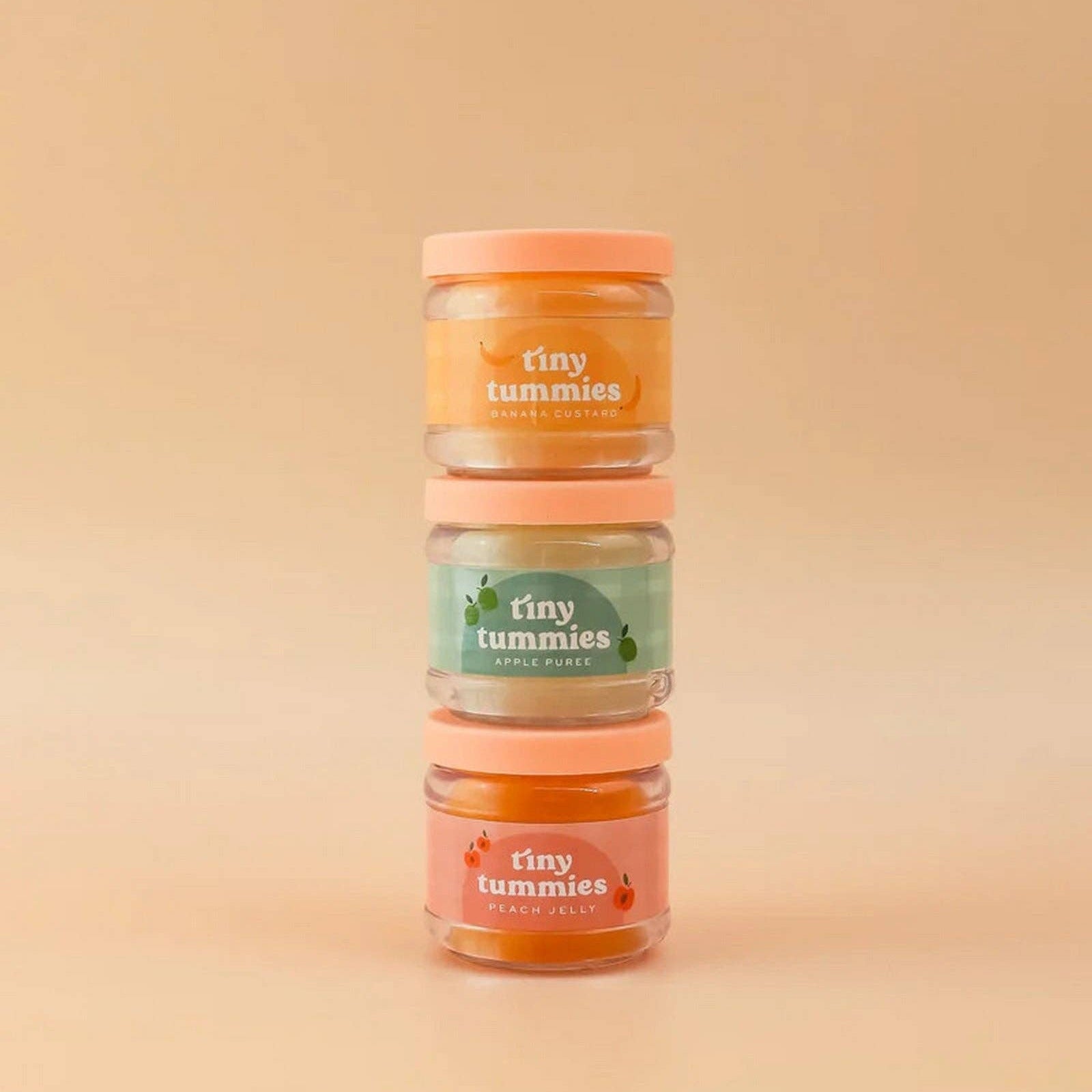 Three jars of 'tiny tummies' baby food on a beige background