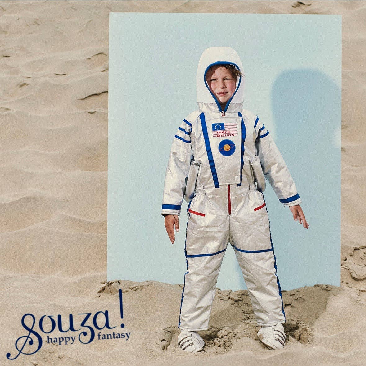 Child in an astronaut suit standing on sand with a blue sky background, featuring the brand 'souza! happy fantasy'.