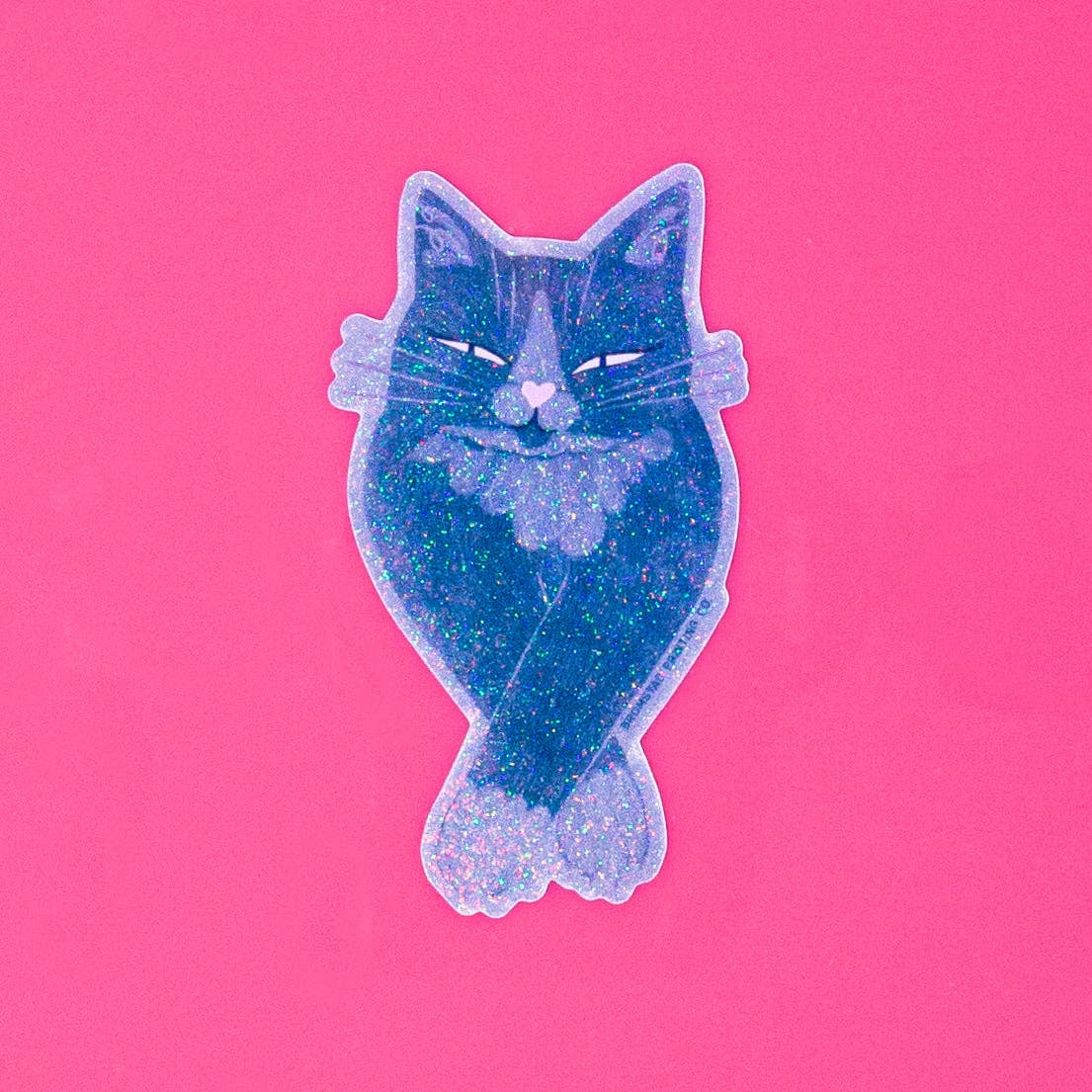 A glittery cat-shaped sticker or patch in shades of blue and purple with a holographic outline, centered on a solid pink background.