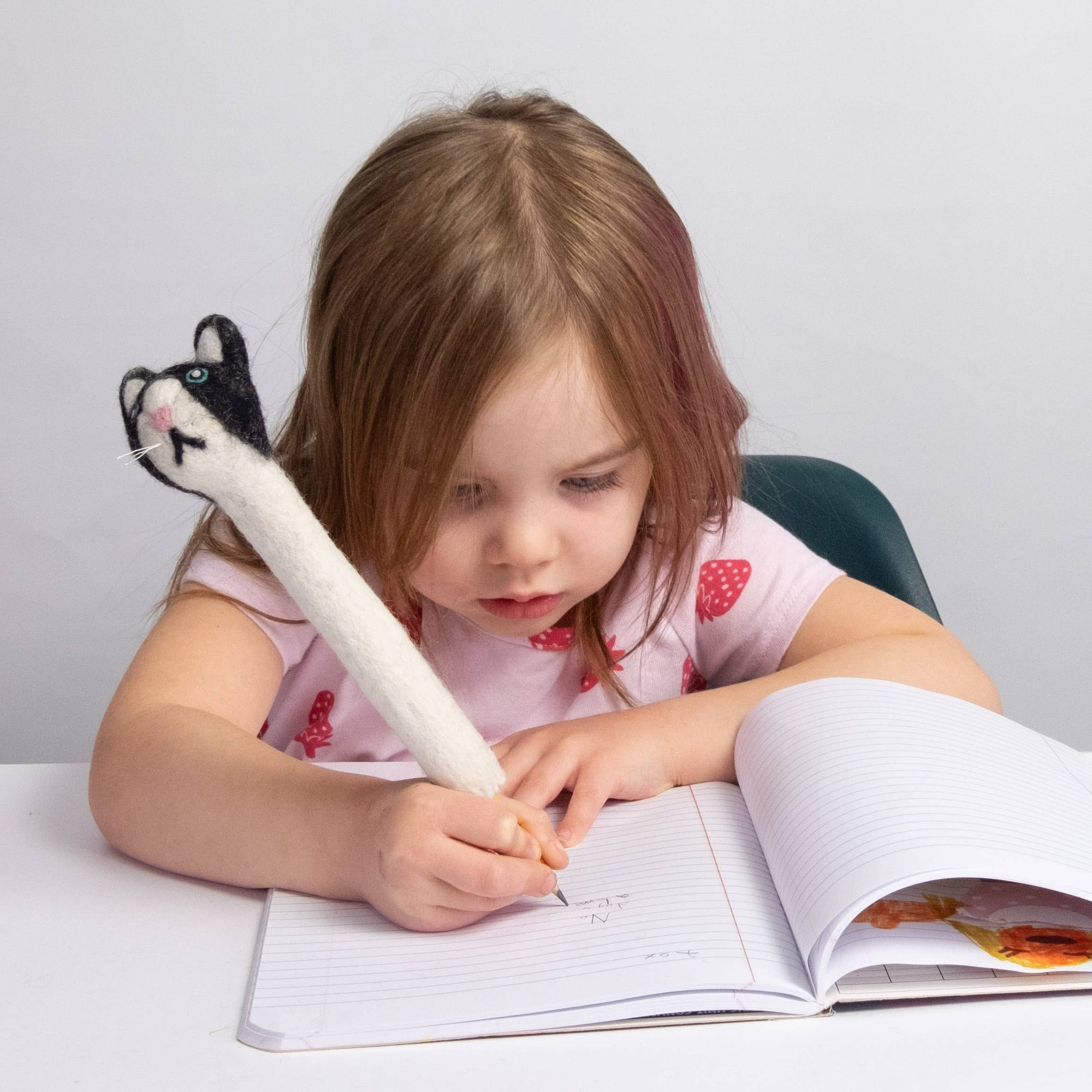 Child writing in a notebook with a stuffed animal pen on a light background