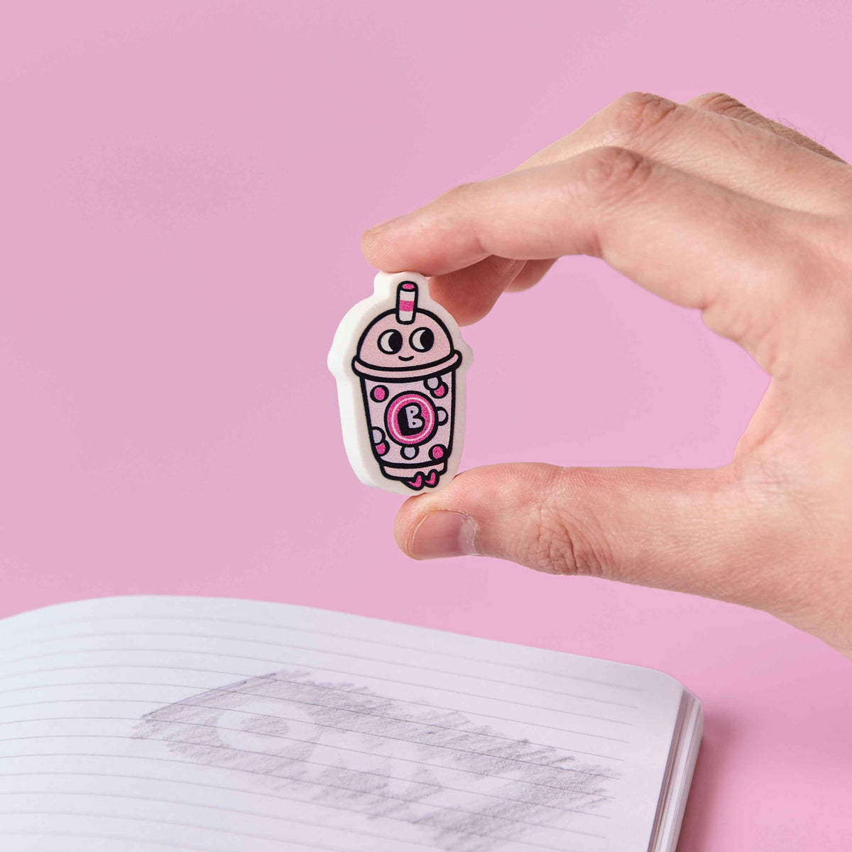 Hand holding a cartoon ice cream cone-shaped eraser over an open notebook with a pink background