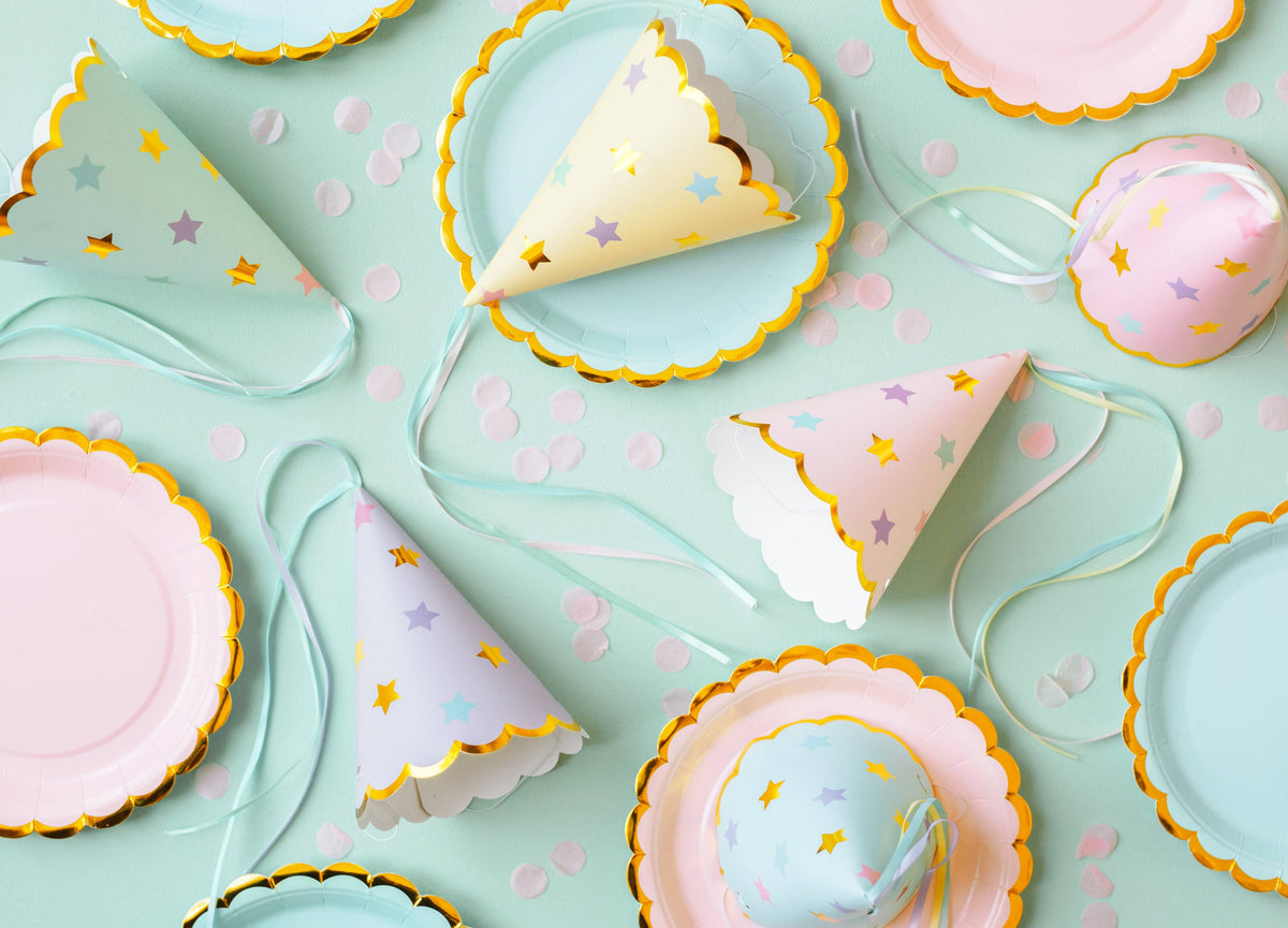 Colorful party hats and plates on a light blue background with confetti.
