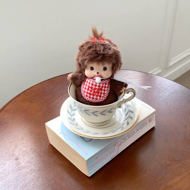 Small plush toy in a teacup on top of a book on a wooden surface