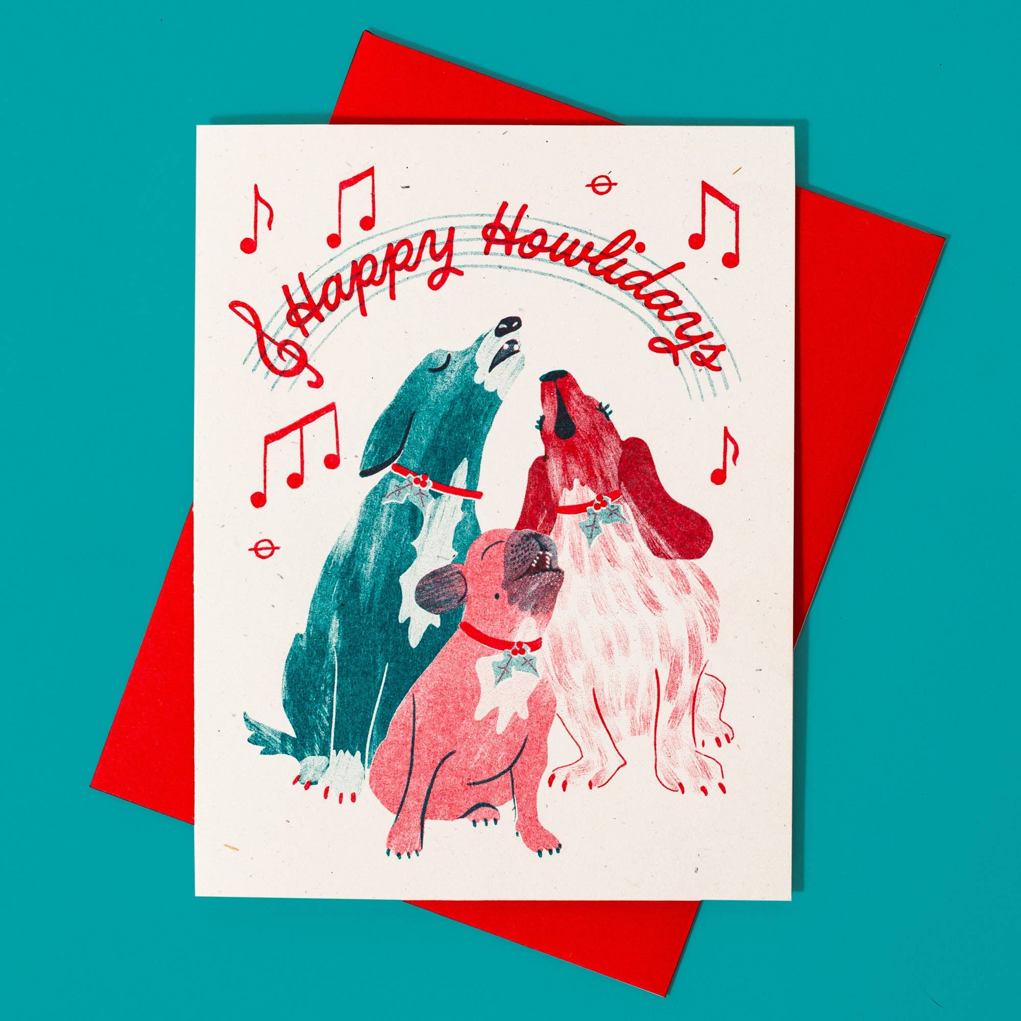 Greeting card with dogs and 'Happy Howlidays' text on a red envelope against a teal background