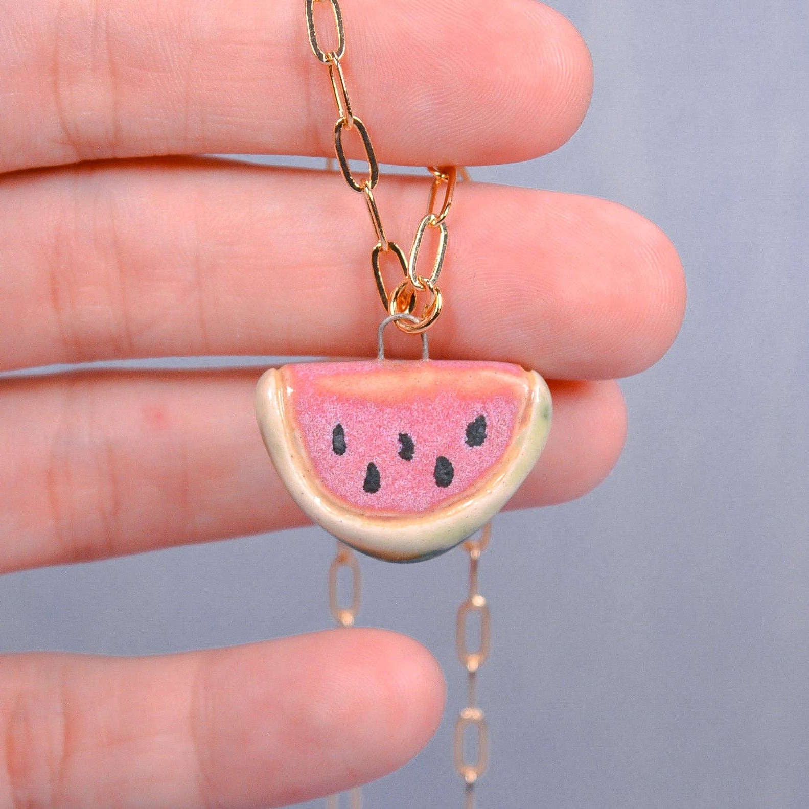 Watermelon slice necklace held between fingers against a neutral background