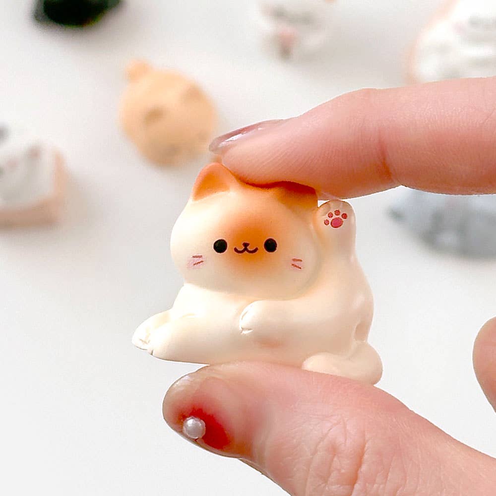 Small white cat figurine held between fingers with a blurred background