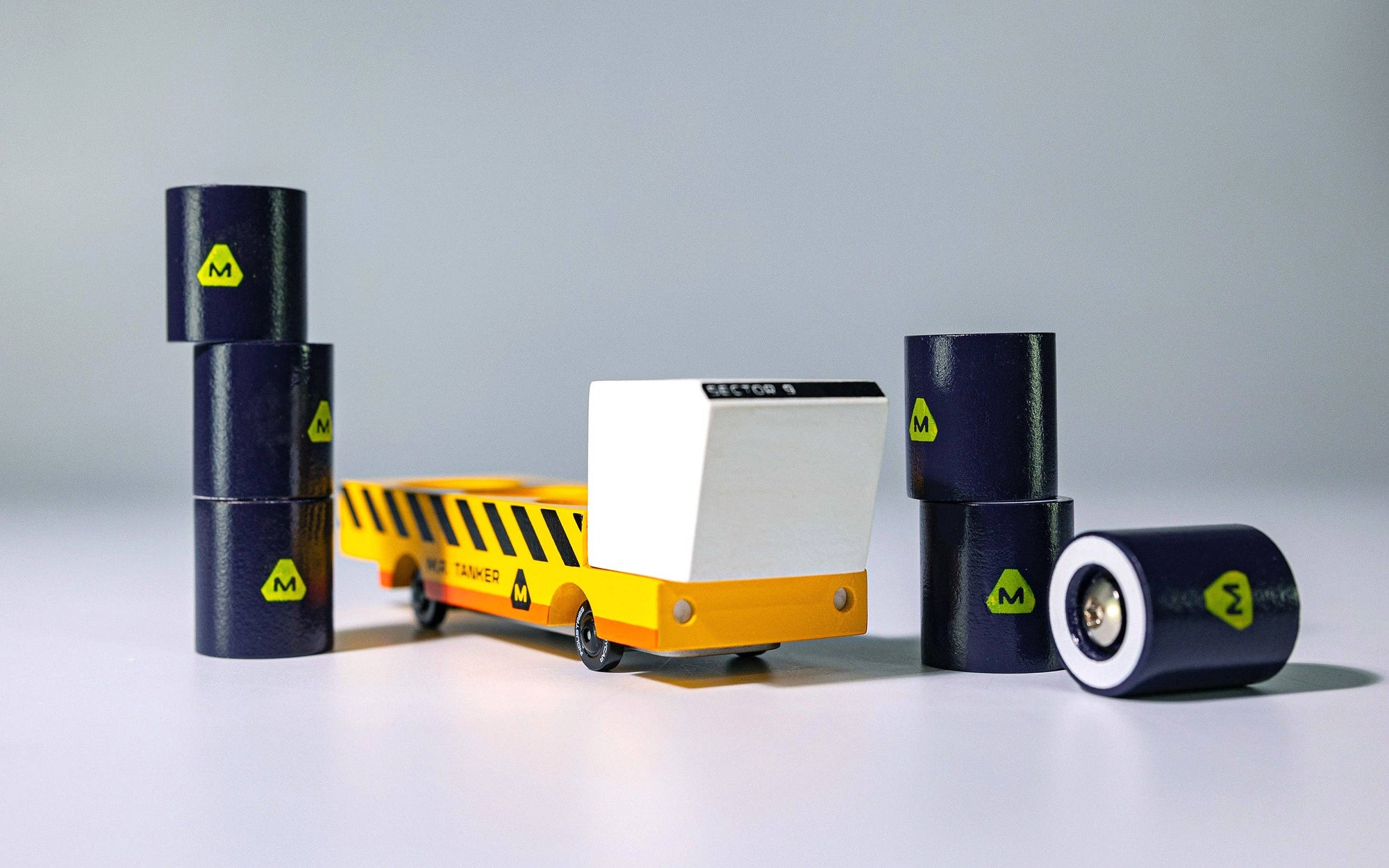 Small yellow and white train model with black cylindrical containers on a gray background