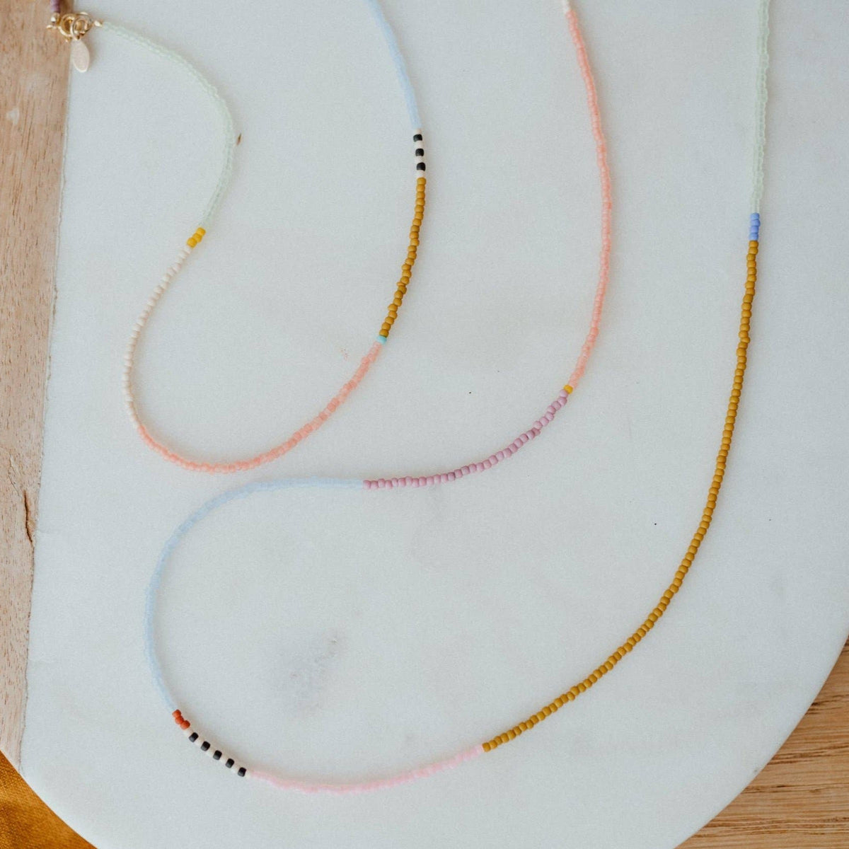 Colorful beaded necklaces on a white plate with a wooden surface underneath