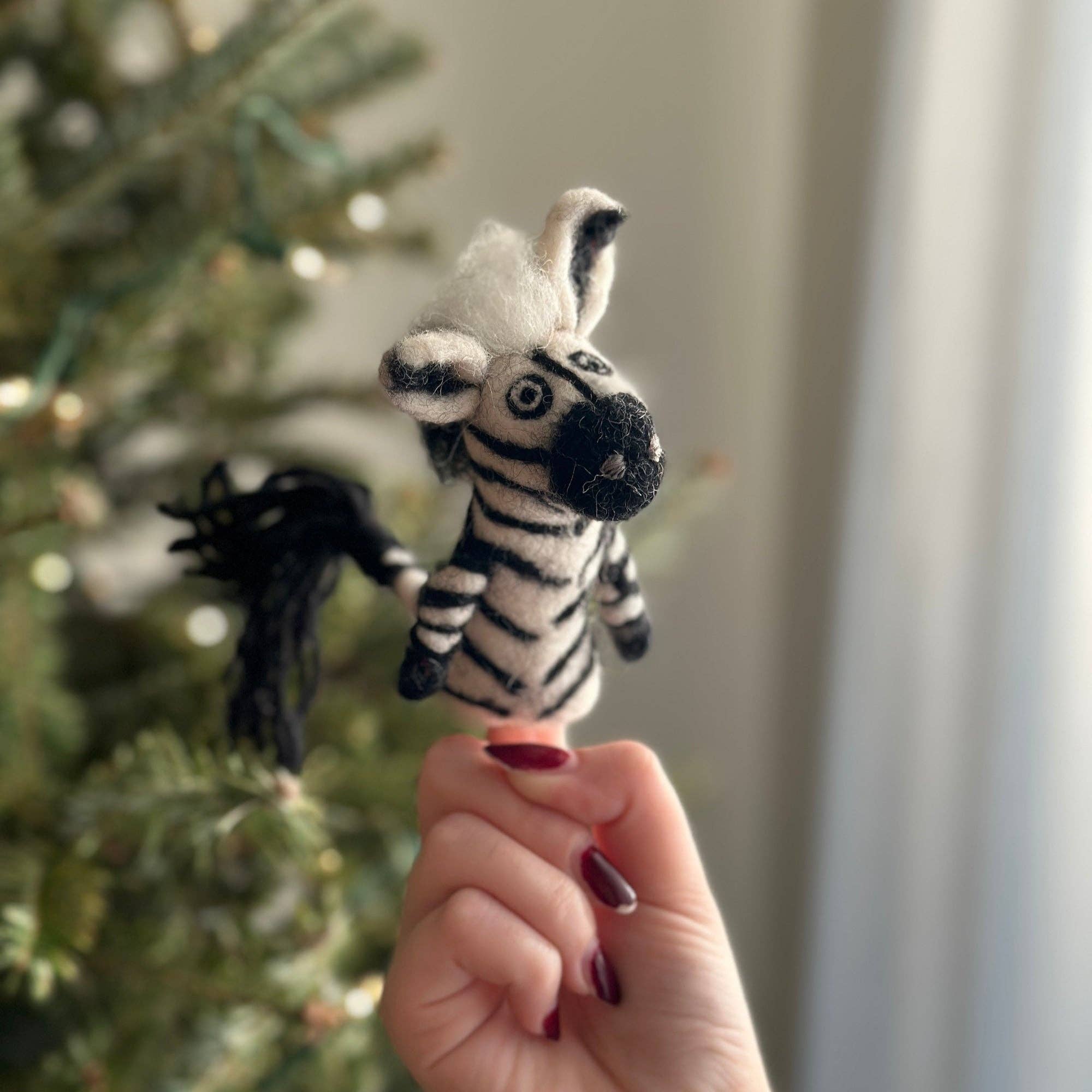 Hand holding a zebra toy in front of a Christmas tree