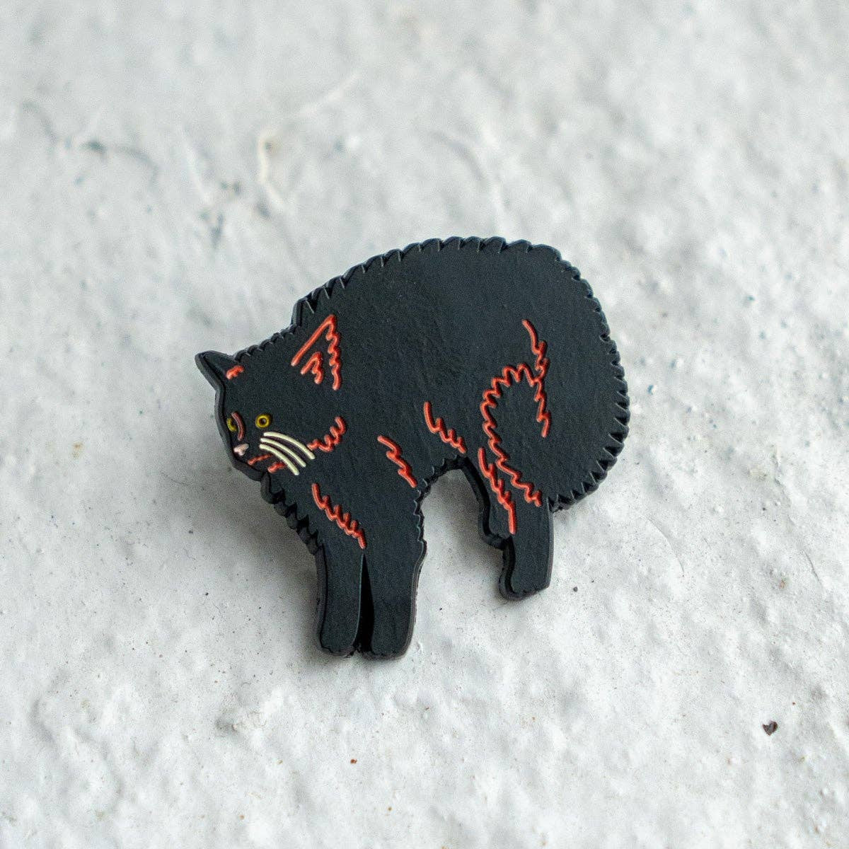 Black cat-shaped pin with red stitching on a textured white surface