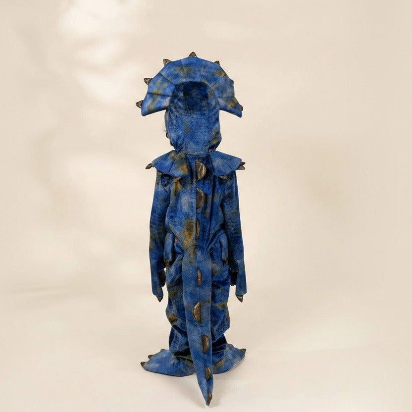 A blue and black textured costume resembling a stylized monster or alien, standing against a plain beige studio background.
